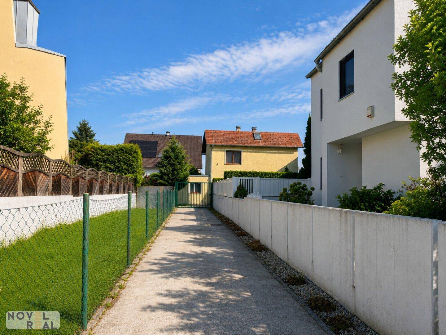Lange Zufahrt zum Grundstück, umgeben von Zäunen und angrenzenden Häusern.