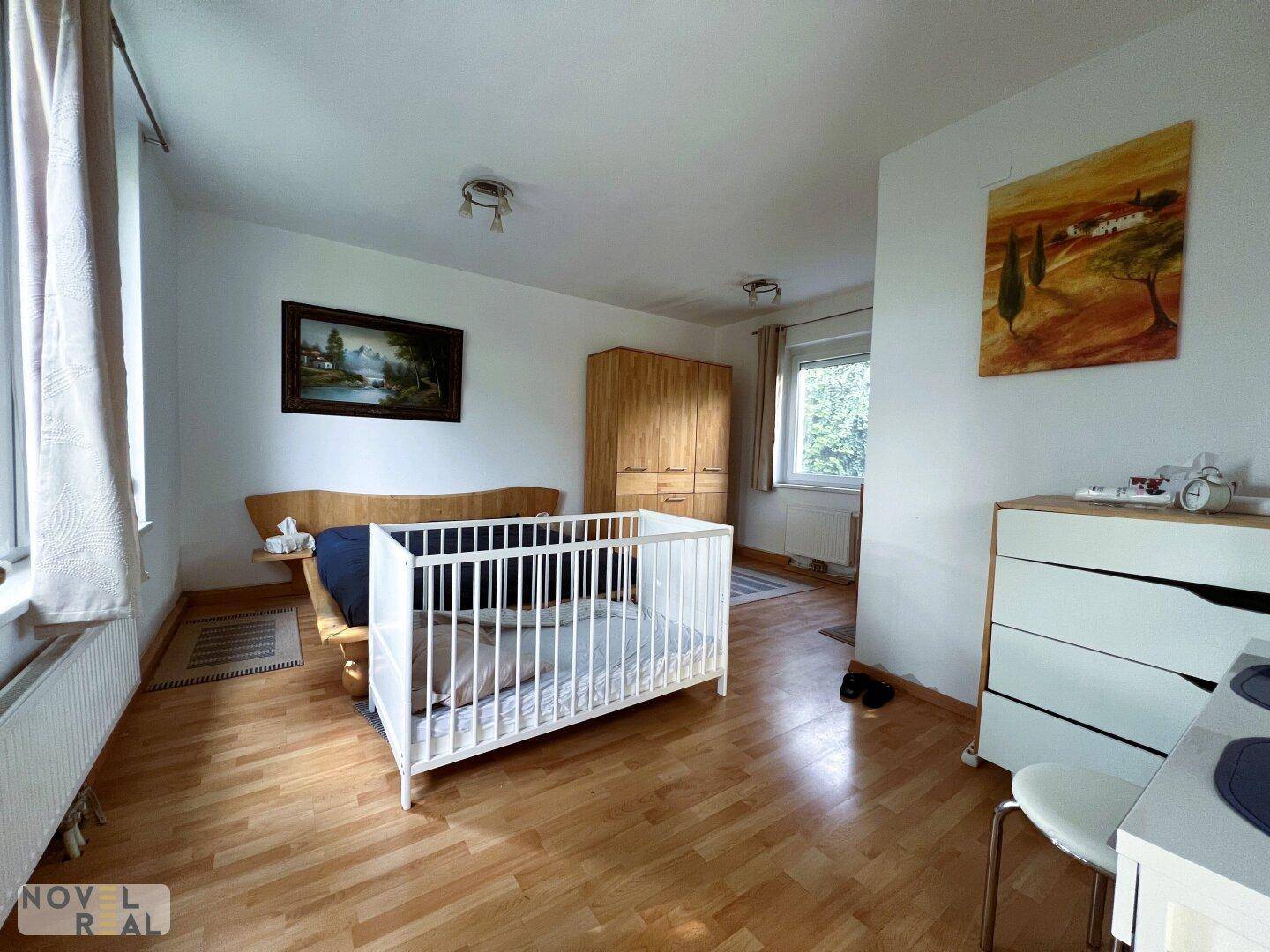 Geräumiges Schlafzimmer mit Holzboden, zwei Fenstern und Platz für ein Kinderbett.
