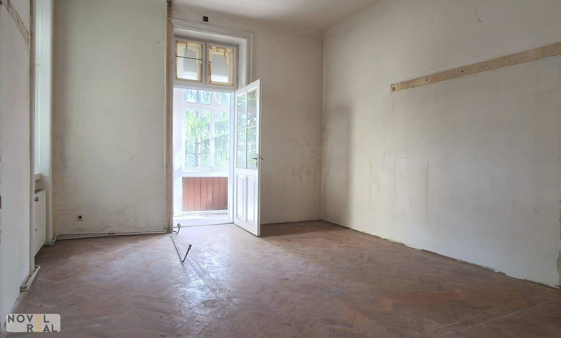 Leeres Zimmer mit Fischgrätparkett und direktem Zugang zu einem Balkon oder einer Loggia.