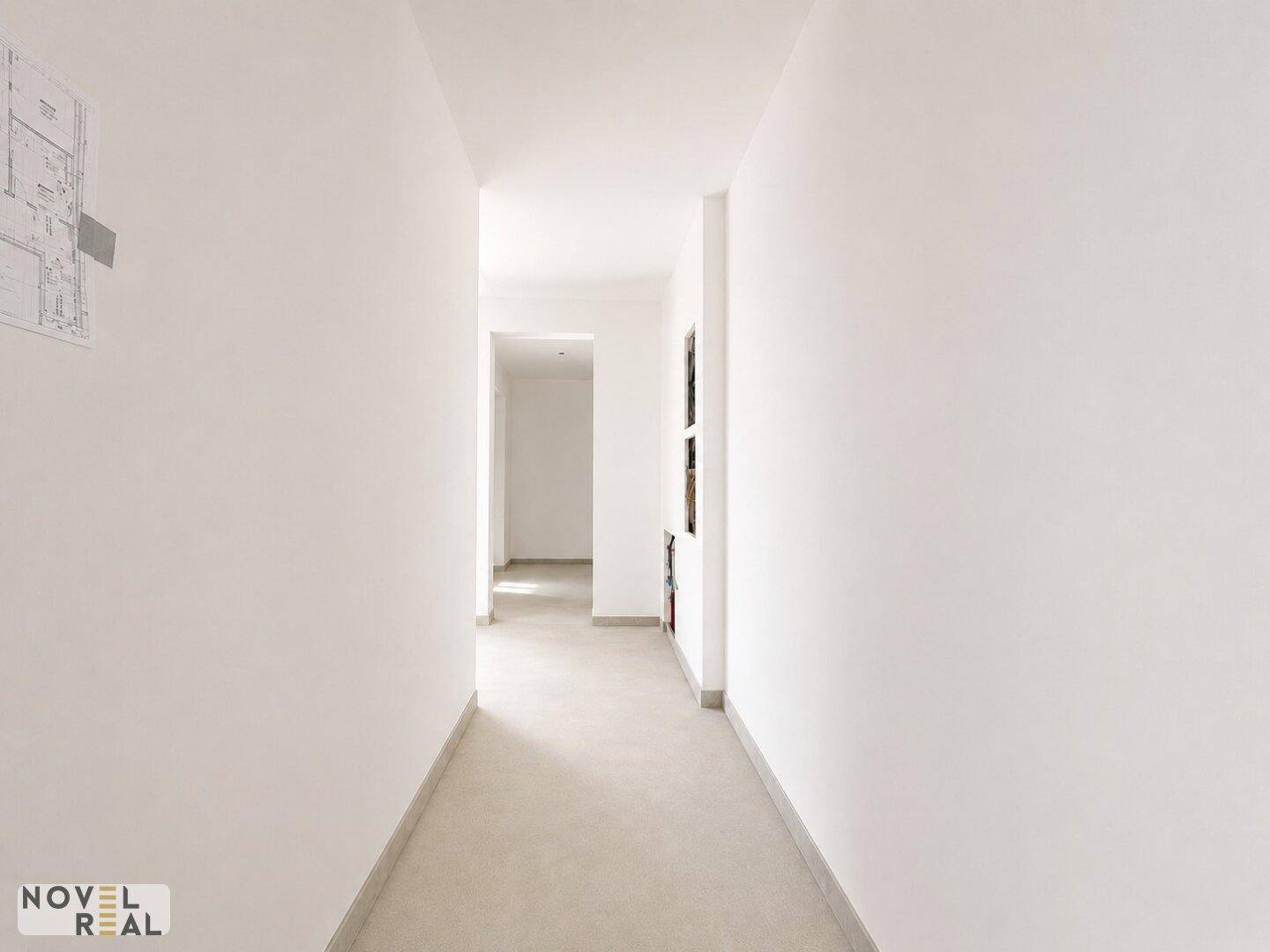 Langer, heller Flur mit weißen Wänden und schlichtem Bodenbelag, führt zu weiteren Räumen der Wohnung.