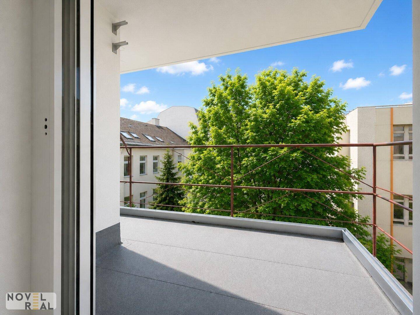 Unmöblierter Balkon mit Blick auf grüne Bäume und umliegende Gebäude, bietet Platz im Freien.