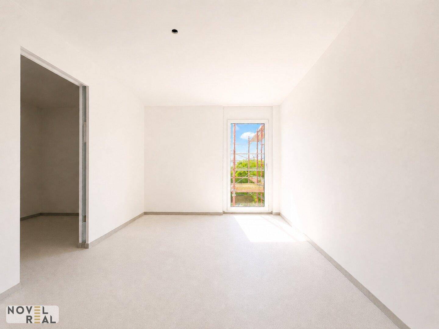 Leerer Raum mit weiß gestrichenen Wänden und einem hohen Fenster, das viel Tageslicht hereinlässt.