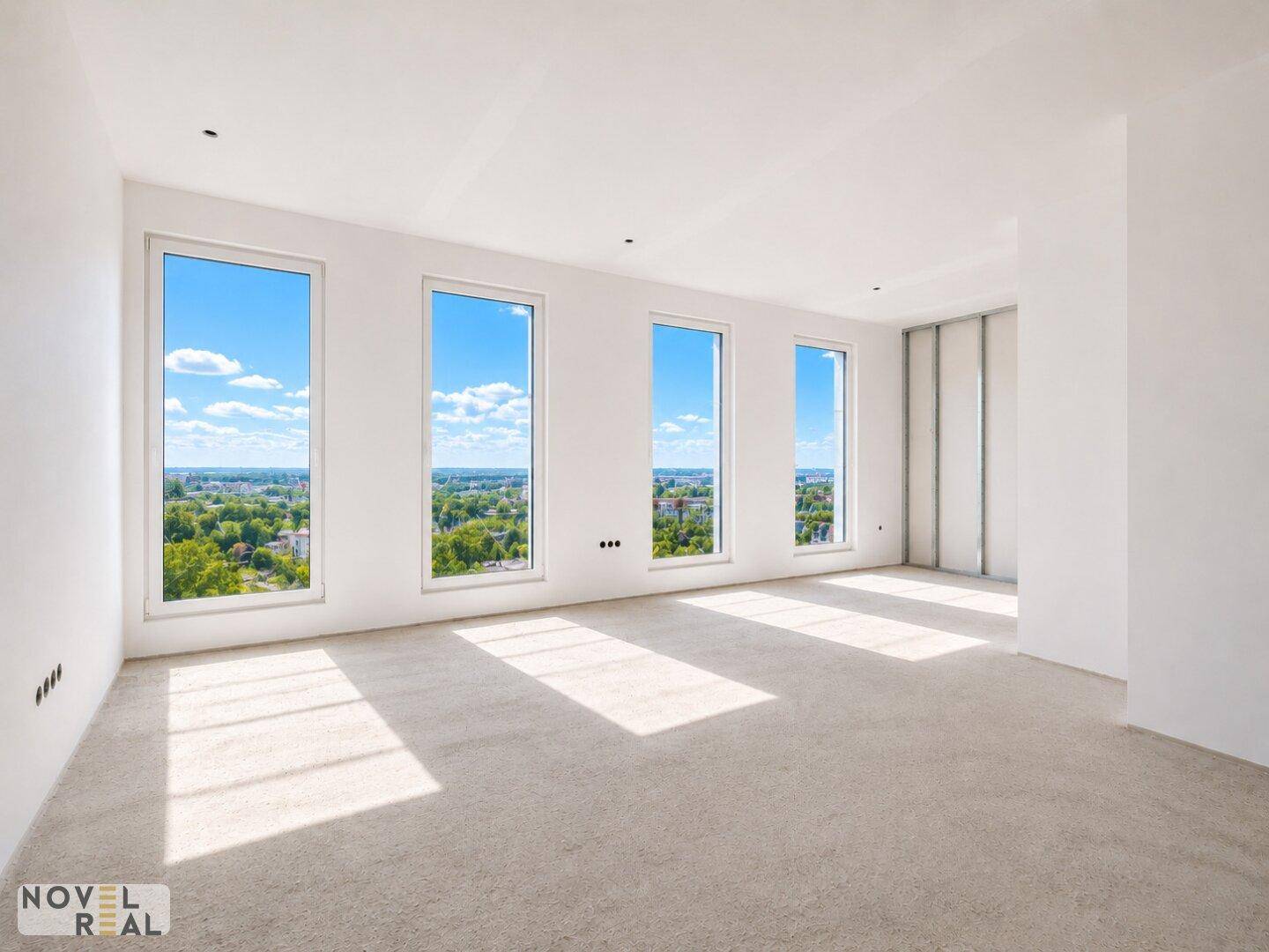 Lichtdurchfluteter Wohnraum mit einer Reihe hoher Fenster und weitem Blick über die grüne Umgebung.