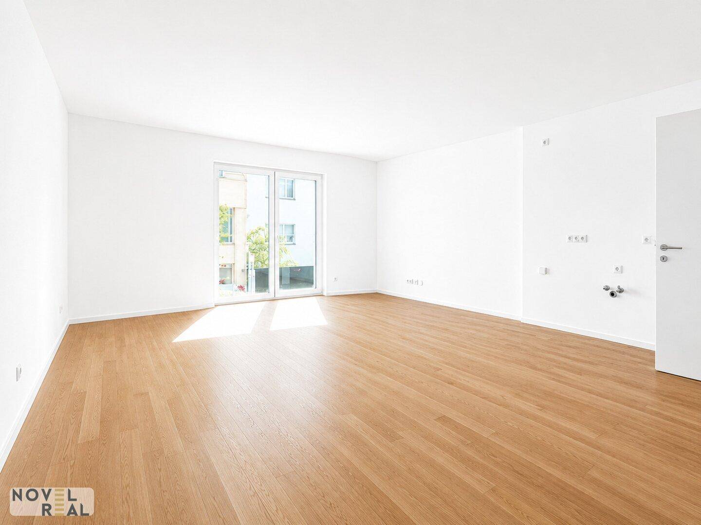 Geräumiger, heller Raum mit Holzboden und Zugang zu einem Balkon oder einer Terrasse.