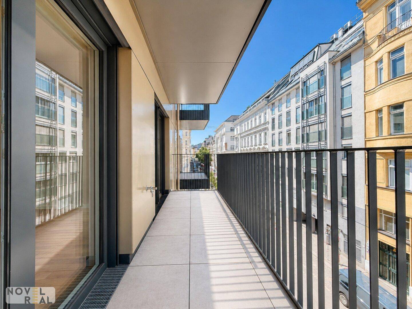 Langer, schmaler Balkon mit Fliesenboden und Blick auf die belebte Stadtstraße und umliegende Gebäude.