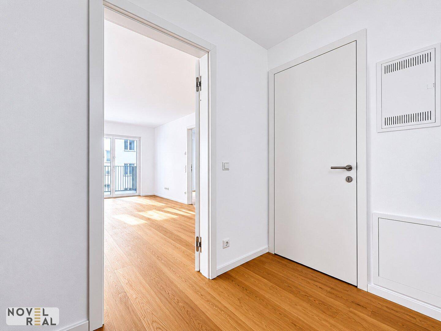 Heller Flur mit Eichenparkettboden, weißen Wänden und offenem Zugang zu einem weiteren Wohnbereich.