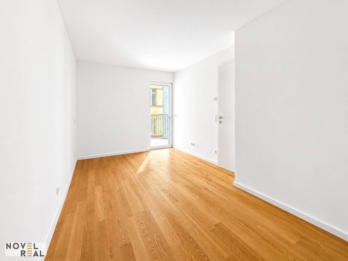 Ruhiges Zimmer mit hellem Parkettboden und Zugang zu einem kleinen Balkon, ideal als Schlafzimmer.