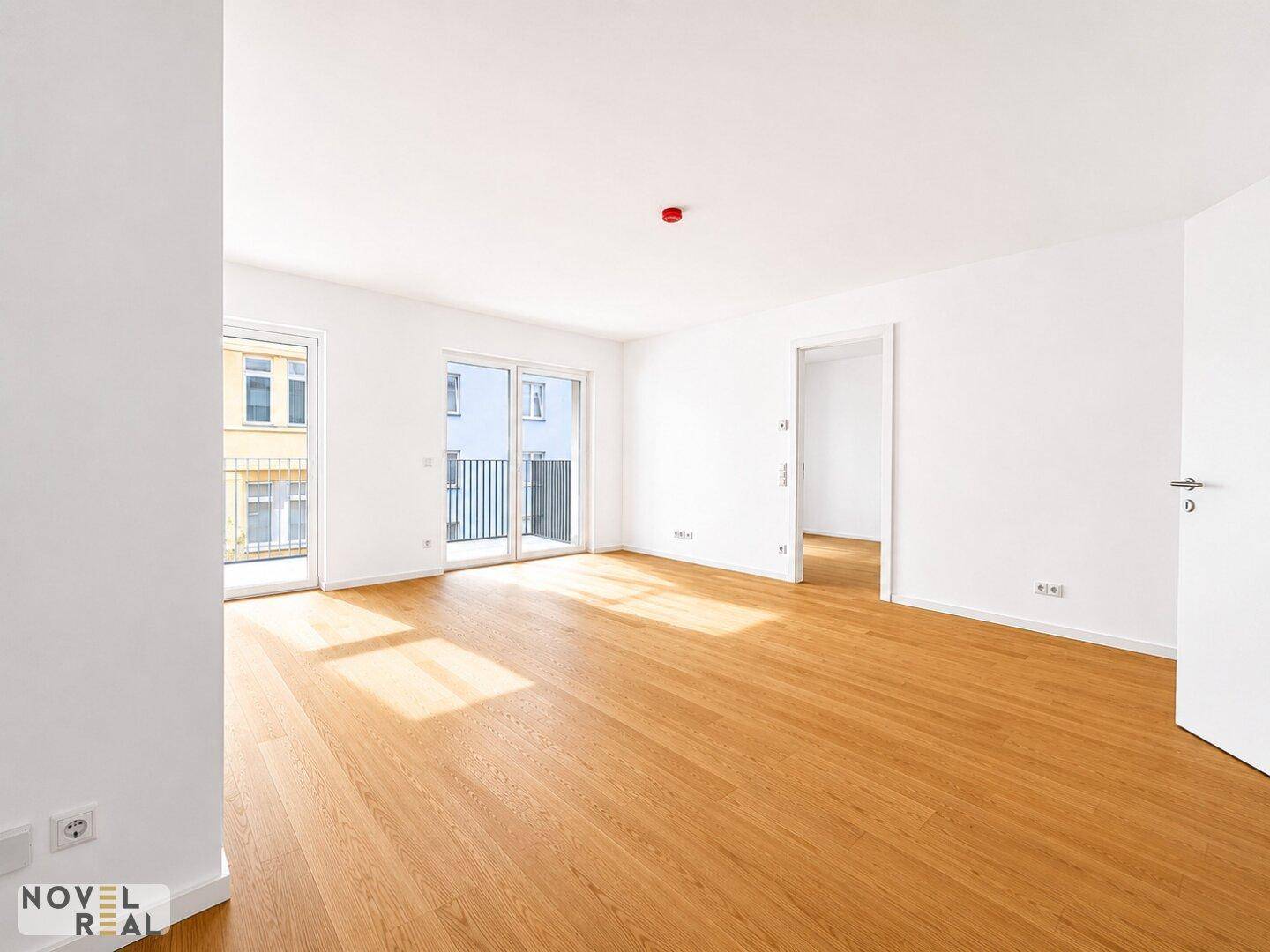 Geräumiger, unmöblierter Wohnbereich mit hellem Parkettboden und viel Tageslicht durch die Balkontüren.