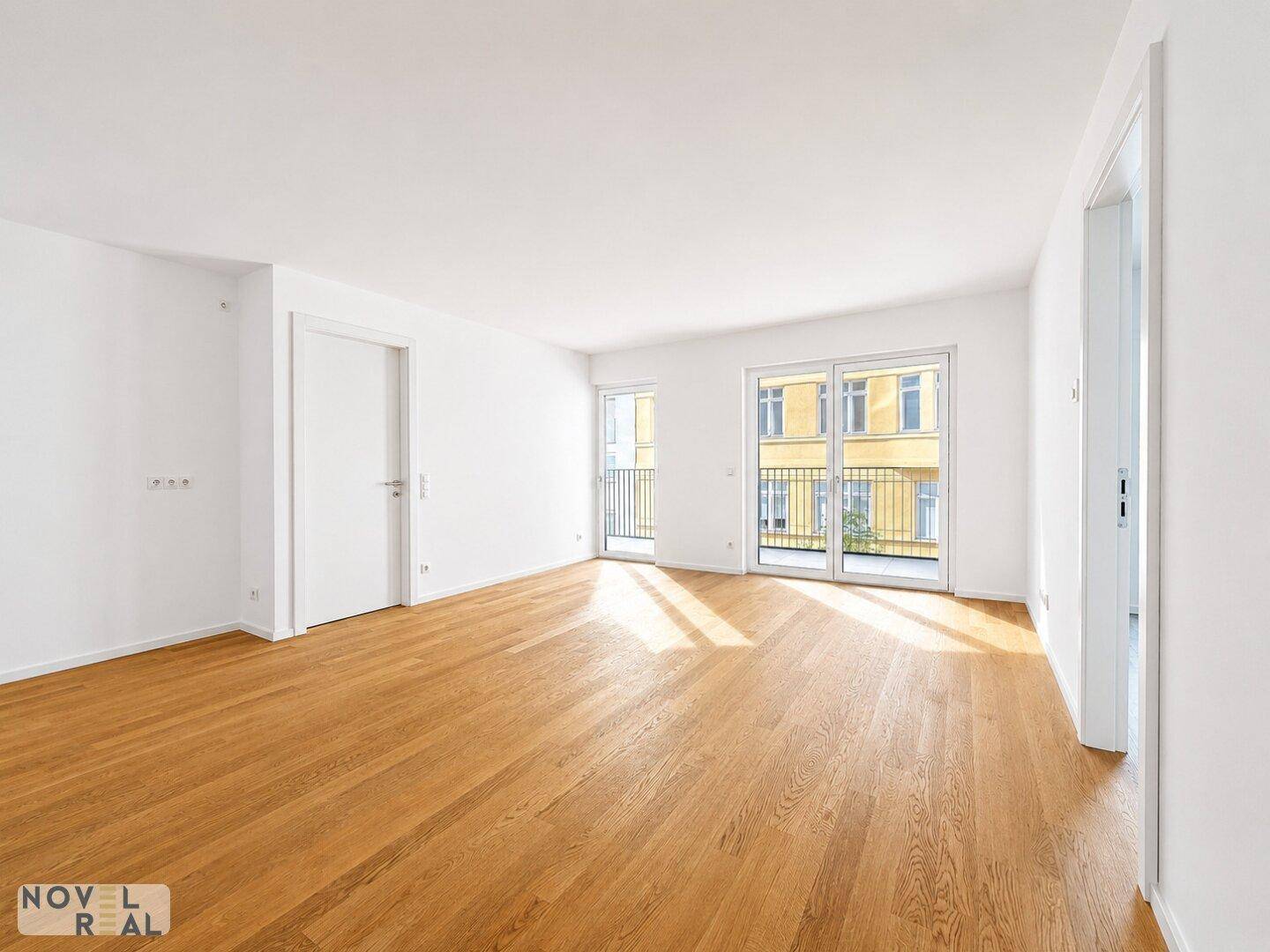 Lichtdurchfluteter Wohnraum mit elegantem Holzparkett und Zugang zu einem Balkon, ideal für moderne Einrichtung.