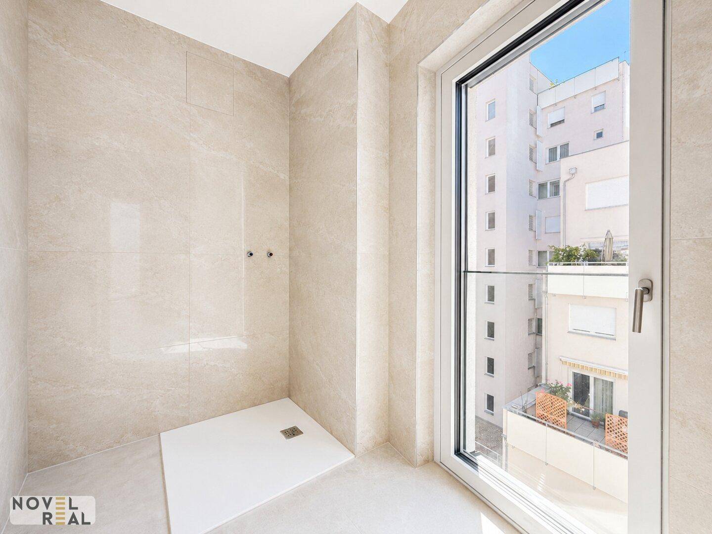 Modernes Badezimmer mit hellen Fliesen, einer begehbaren Dusche und einem Fenster für Tageslicht.