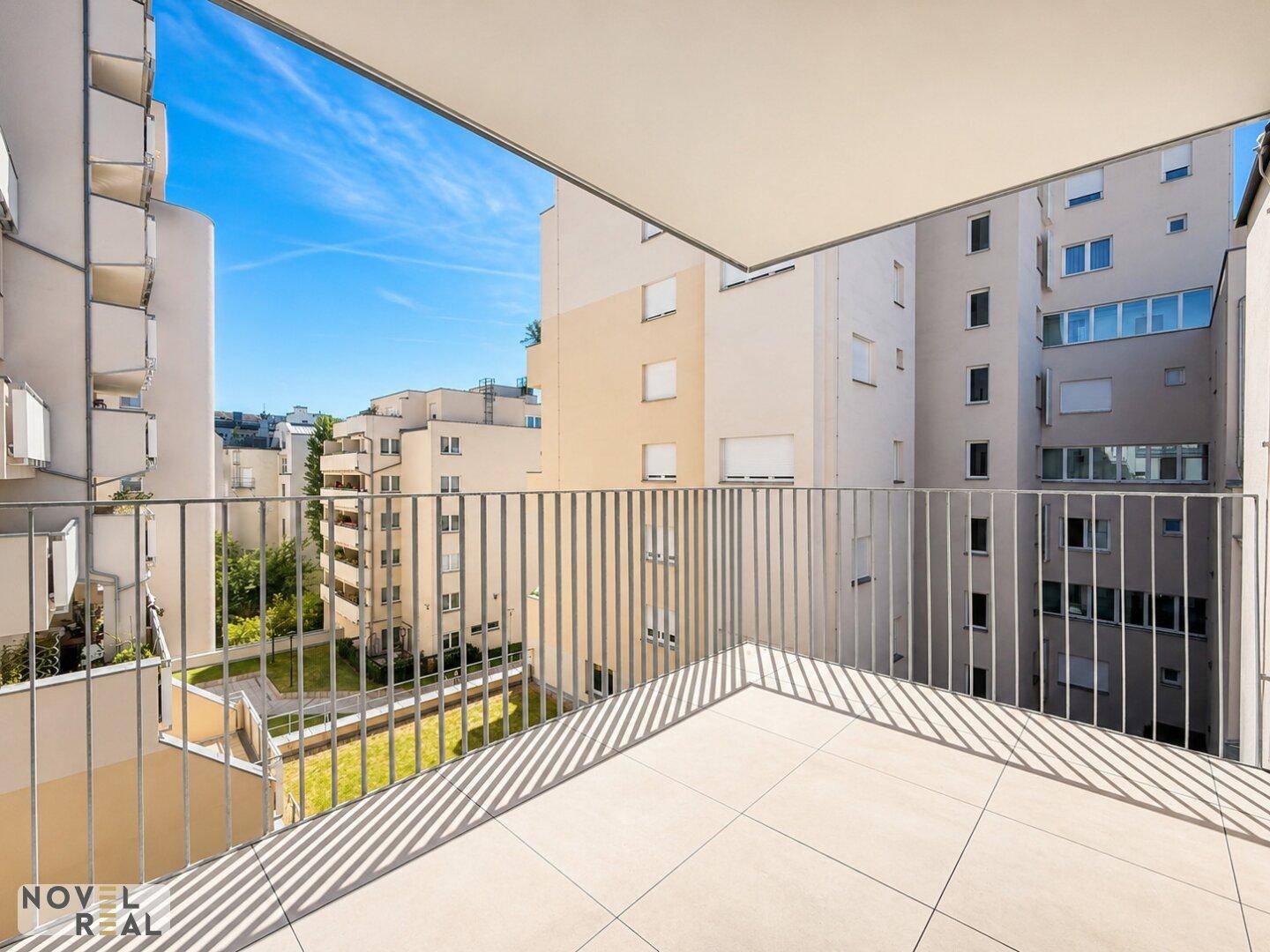 Geräumiger Balkon mit Fliesenboden und Blick auf den begrünten Innenhof und umliegende Gebäude.