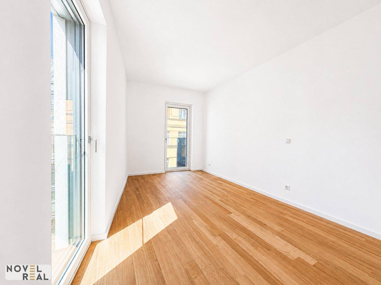 Geräumiges Schlafzimmer mit hellem Parkettboden und viel Tageslicht durch die großen Fenster.