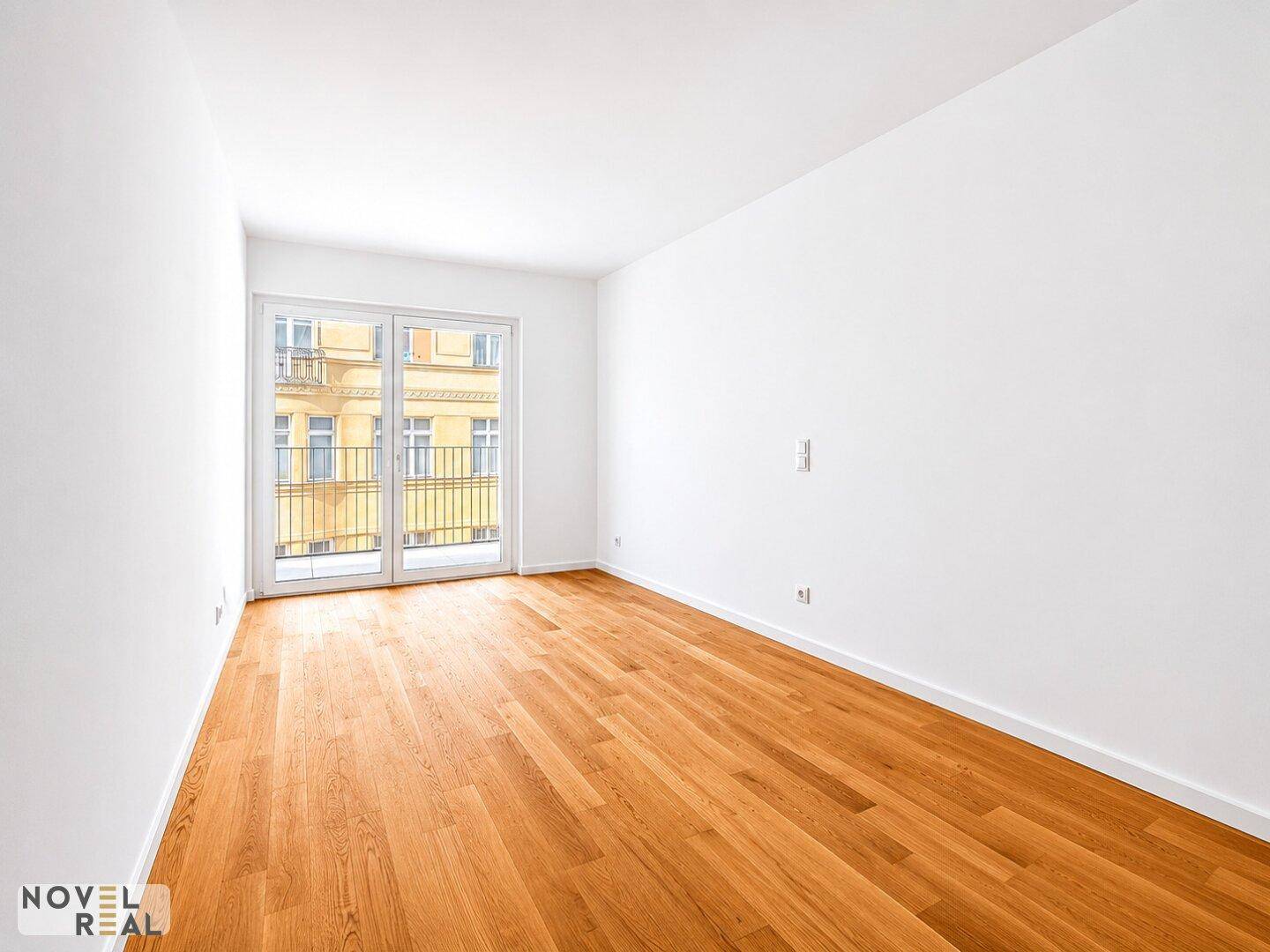 Schlafzimmer mit hellem Parkettboden und einem französischen Balkon, der viel Licht spendet.