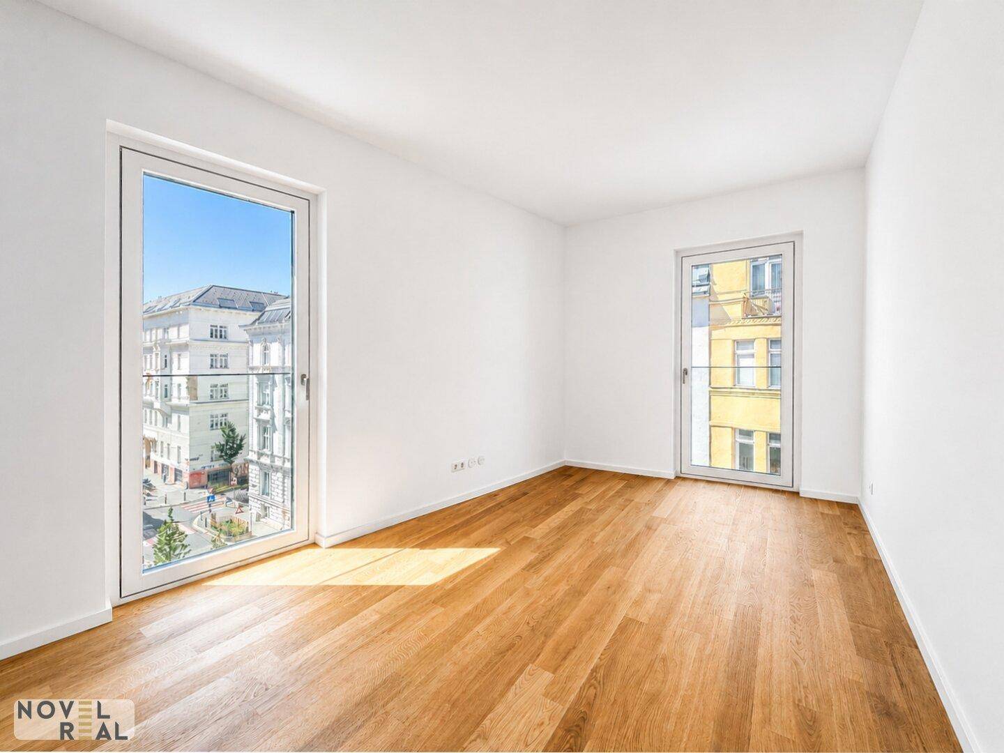 Helles Schlafzimmer mit Parkettboden und großen Fenstern mit Blick auf die Stadtstraße.