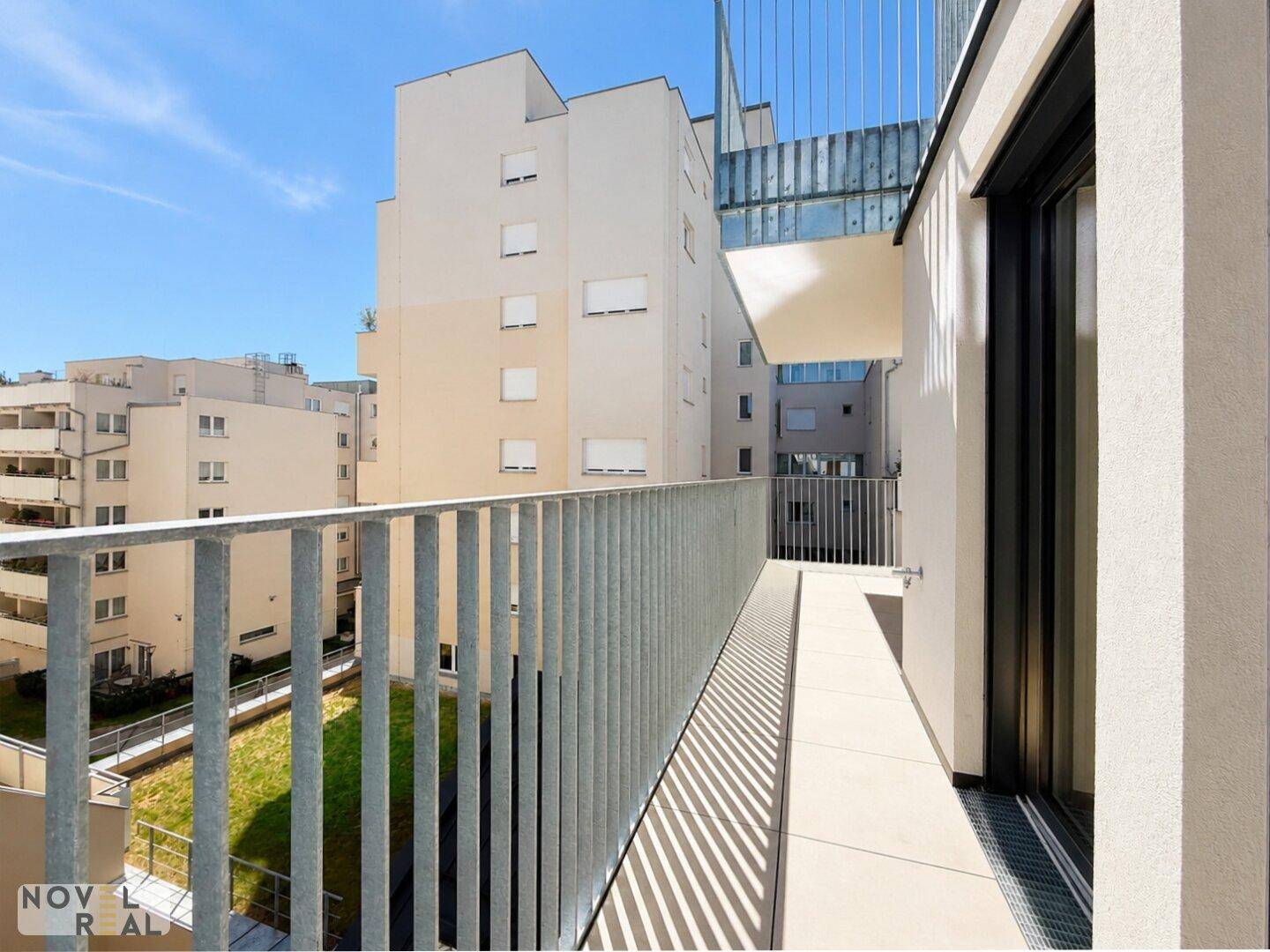 Langer Balkon mit modernem Metallgeländer und Ausblick auf die umliegende Wohnanlage.