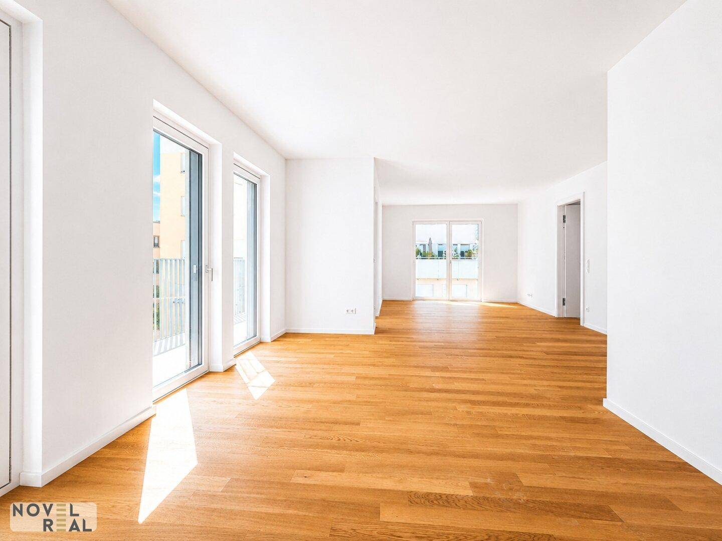 Geräumiges Wohnzimmer mit hellem Holzparkett und großen Fenstern, die viel Tageslicht hereinlassen.