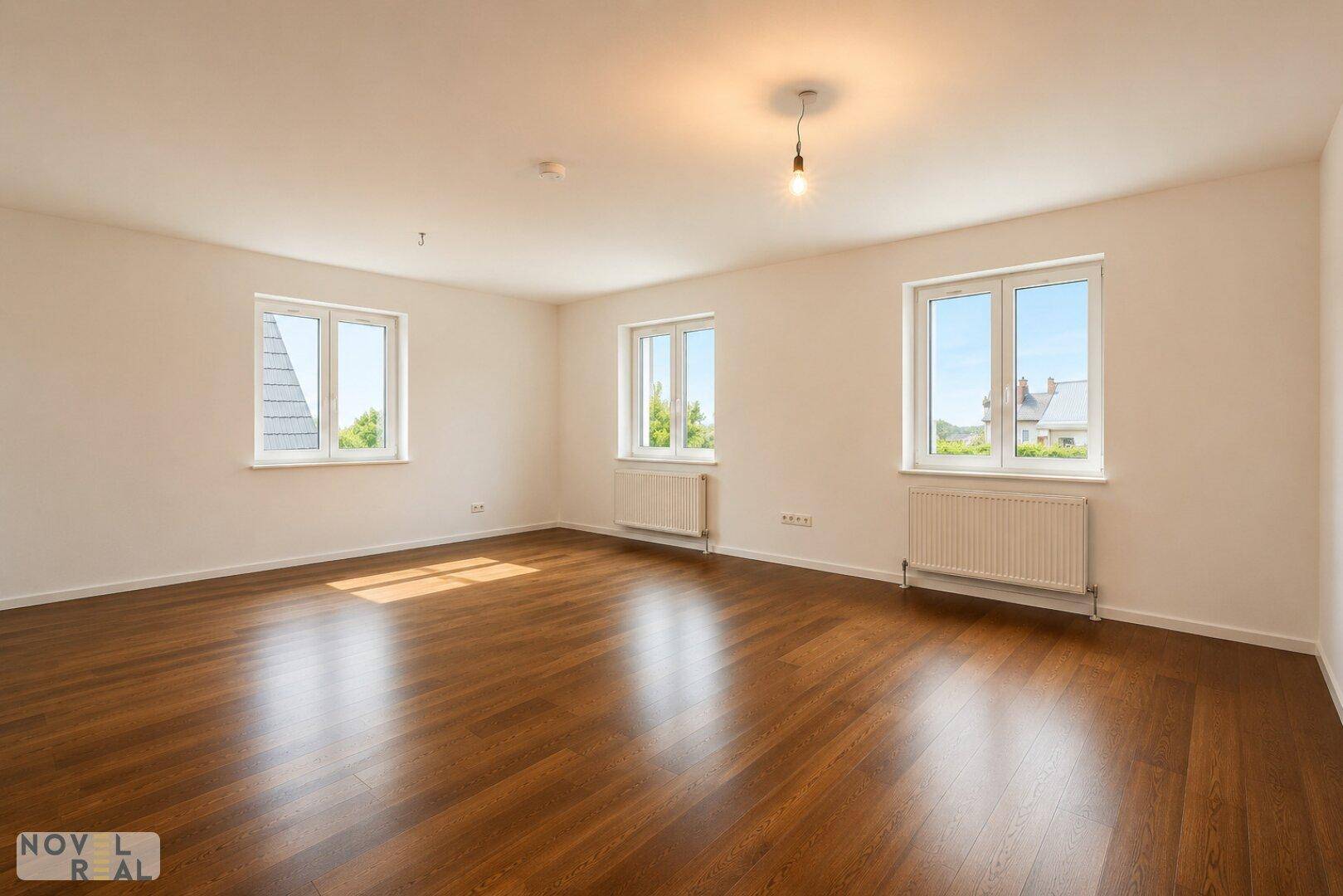 Leerer Raum mit Holzboden, mehreren Fenstern und viel natürlichem Tageslicht.