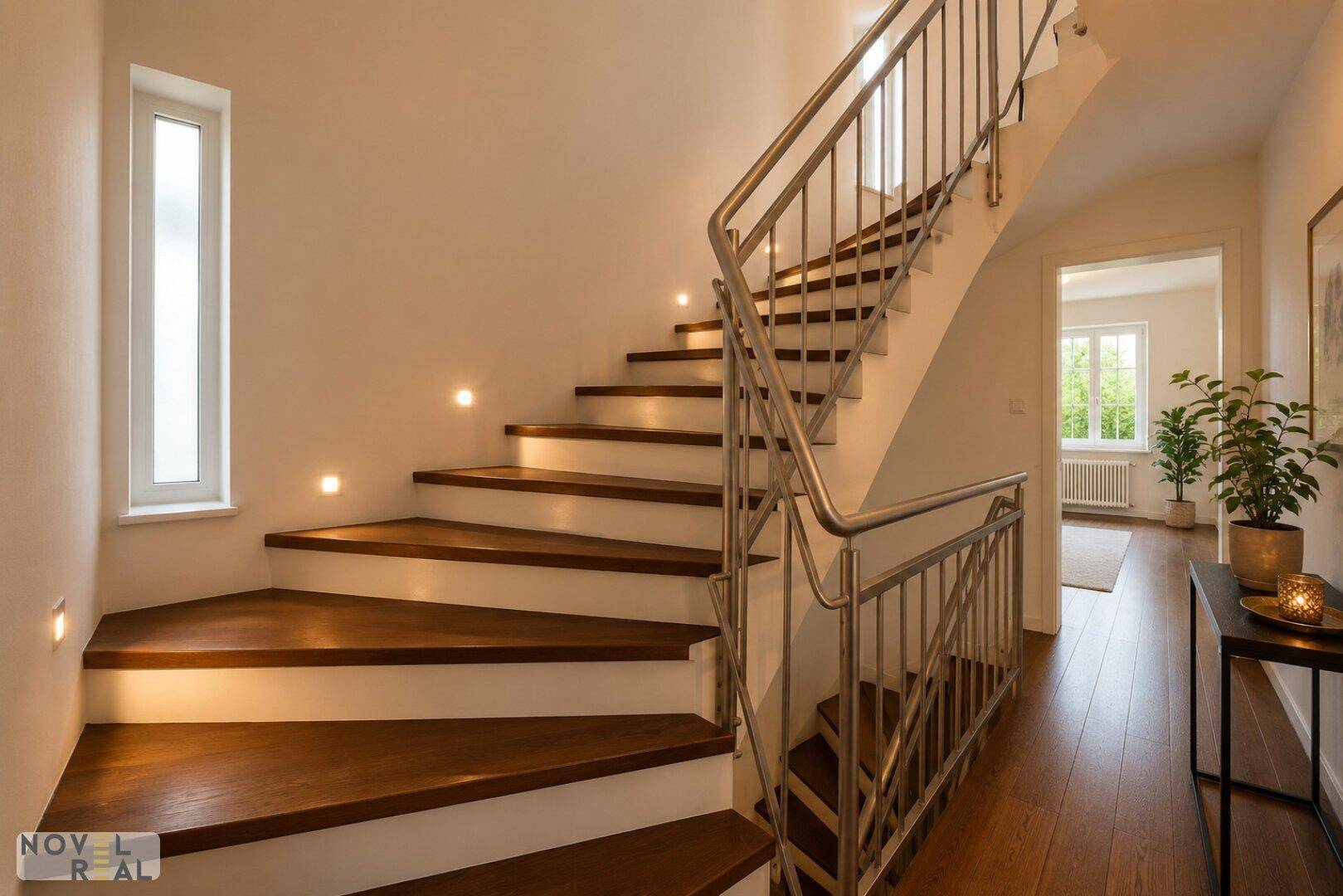 Moderne Holztreppe mit Edelstahlgeländer und indirekter Beleuchtung im Flurbereich.