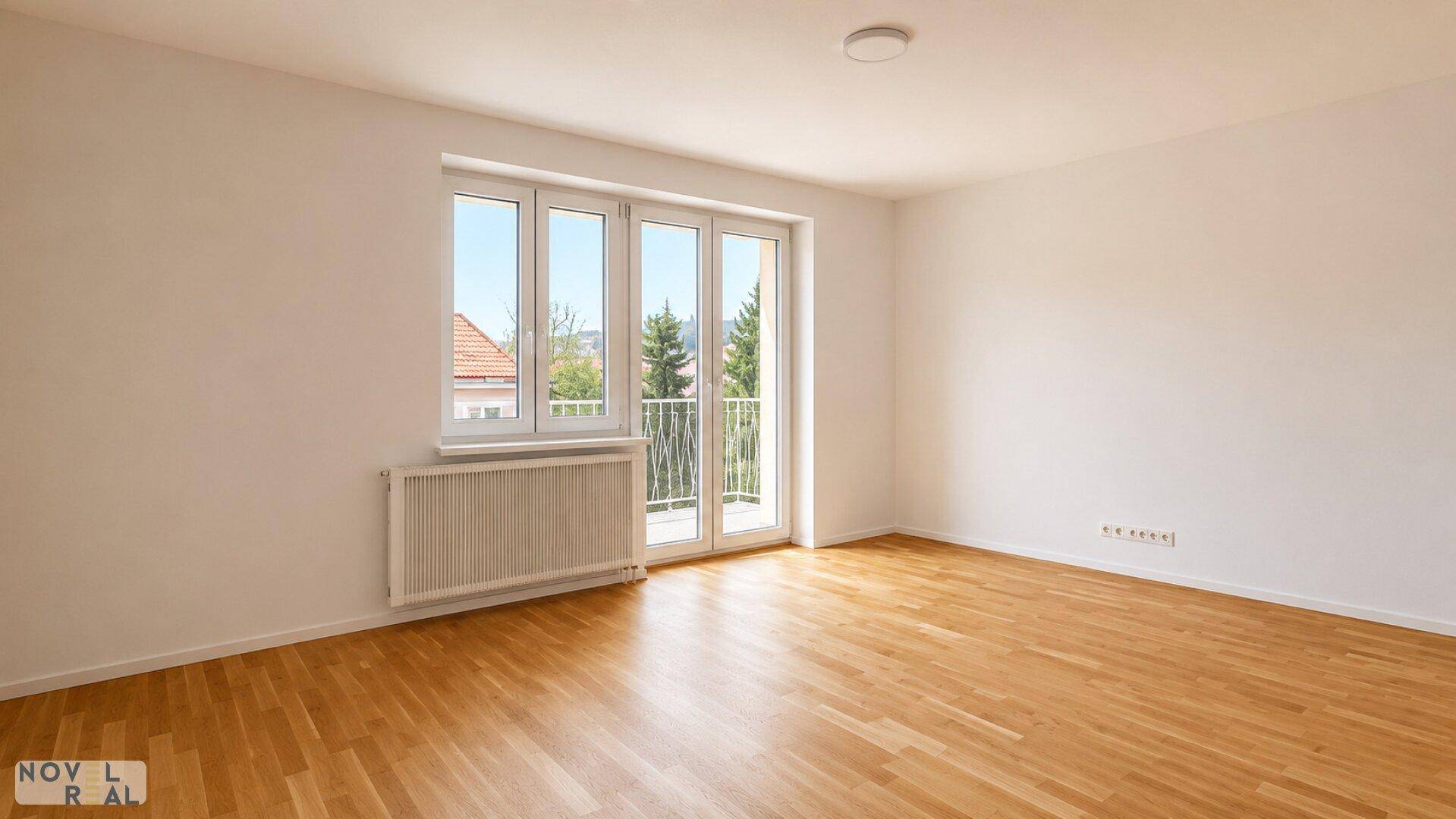 Geräumiges, helles Zimmer mit Holzboden und Blick ins Grüne durch die Fenster.