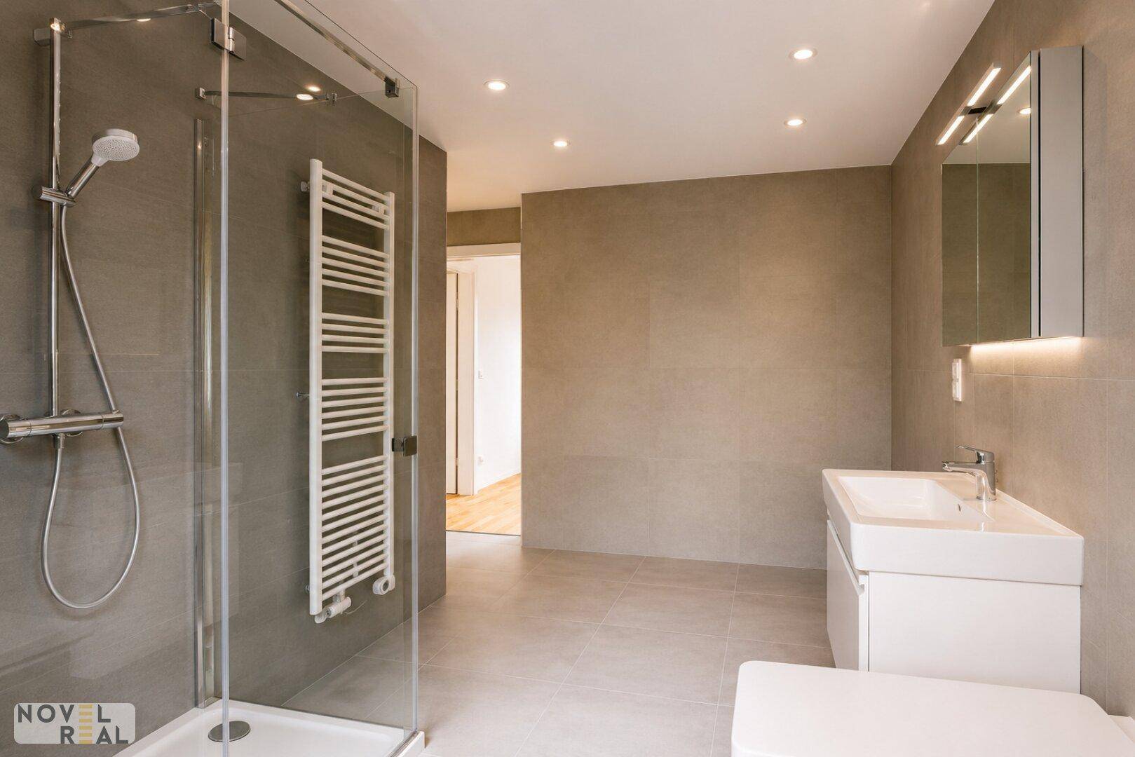 Geräumiges Badezimmer mit moderner Dusche, Waschtisch und Zugang zum Flur.