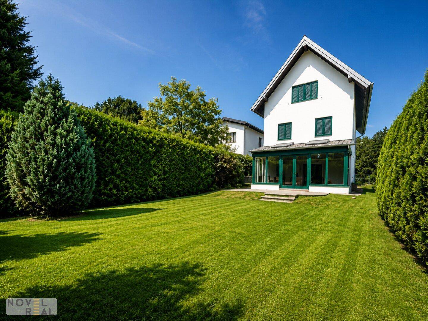 Gepflegter Garten mit Rasenfläche und Blick auf die Rückseite des Hauses mit Wintergarten.