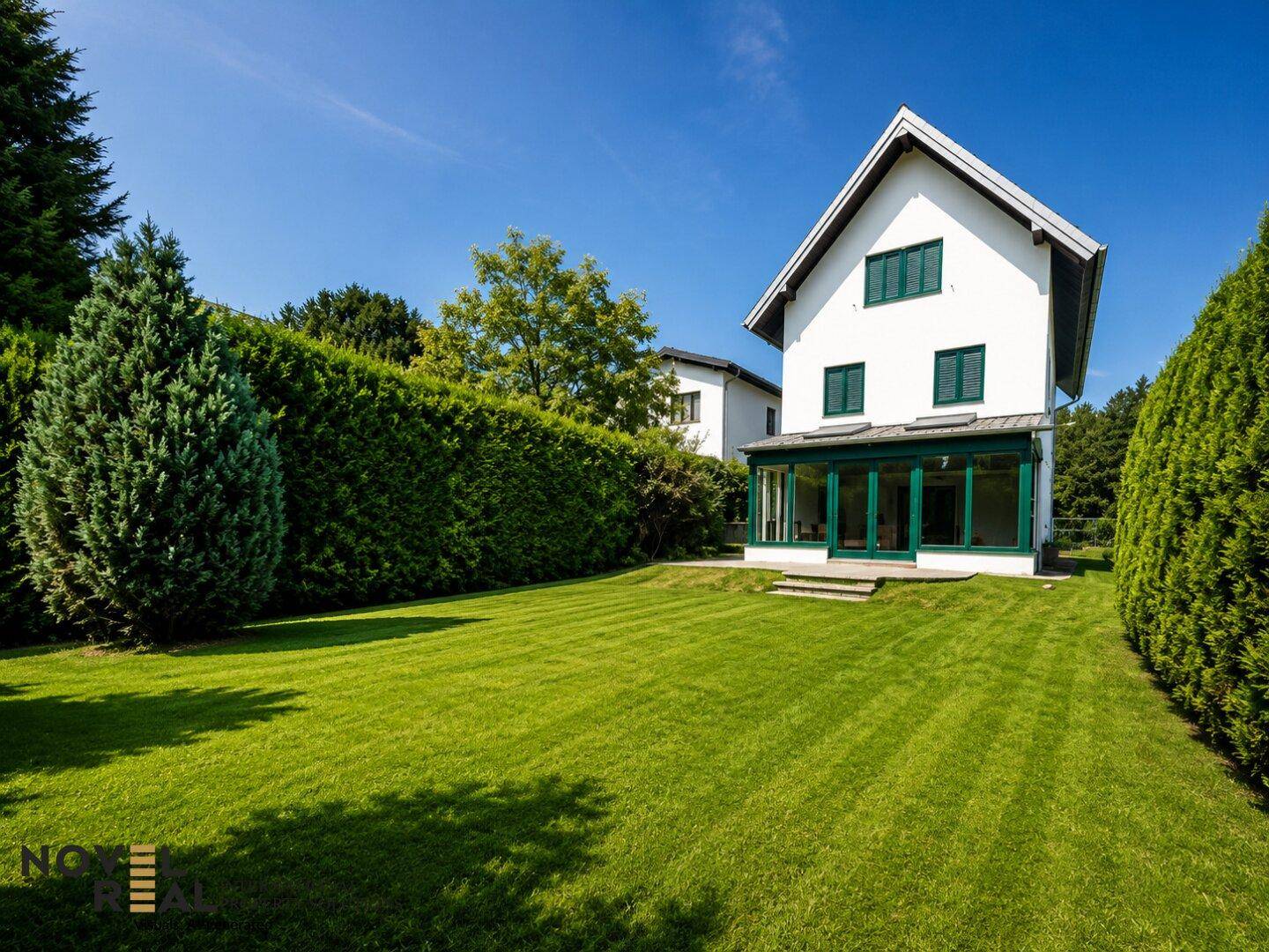 Weitläufiger Gartenbereich mit gepflegtem Rasen und hohen Hecken, die Privatsphäre bieten.