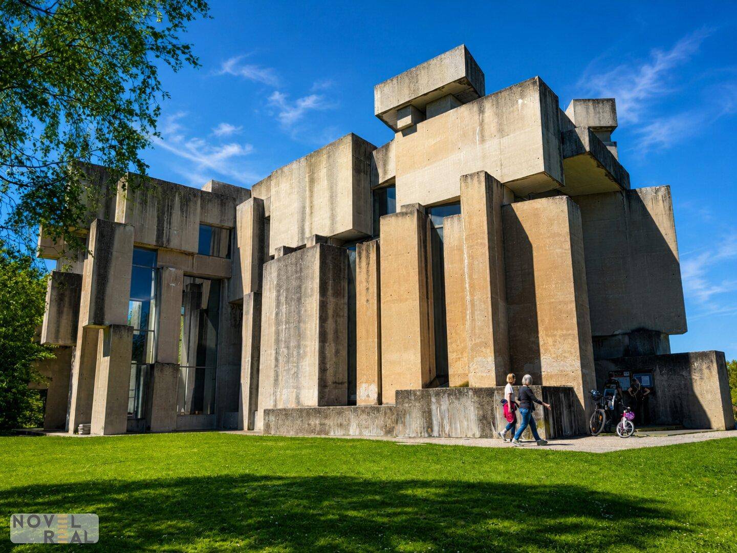 Markantes brutalistisches Gebäude aus Betonblöcken, umgeben von Rasenflächen und Spaziergängern.