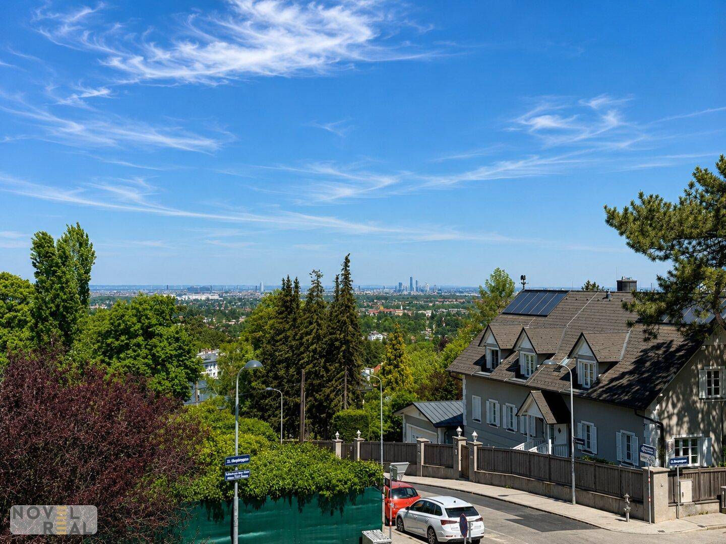 Wohnstraße mit Häusern und einem weiten Blick auf die Stadt, Solaranlage auf einem Dach.