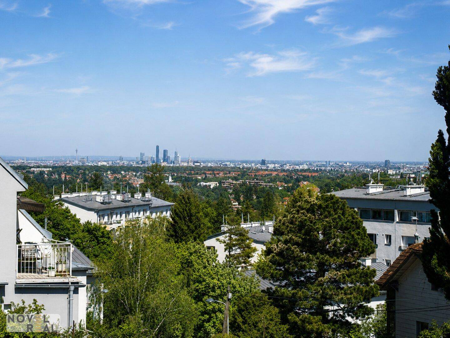 Panoramablick auf die Stadt mit Hochhäusern, Dächern und viel Grün im Vordergrund.