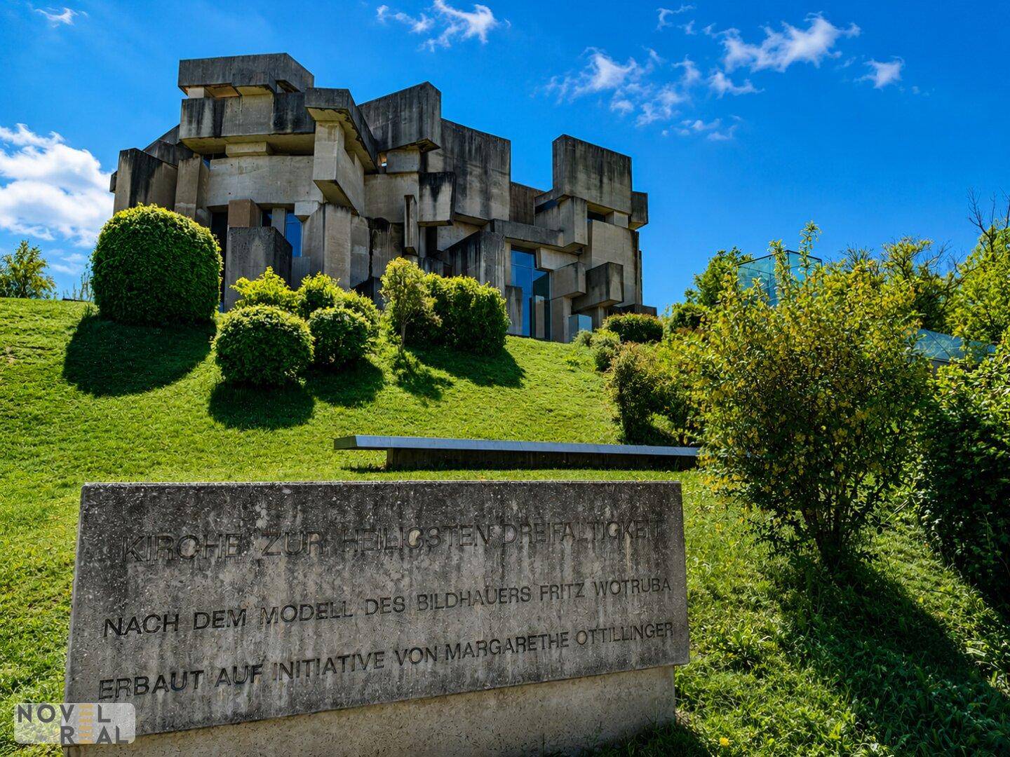 Die Wotruba-Kirche, ein markantes Betongebäude auf einem grünen Hügel unter blauem Himmel.