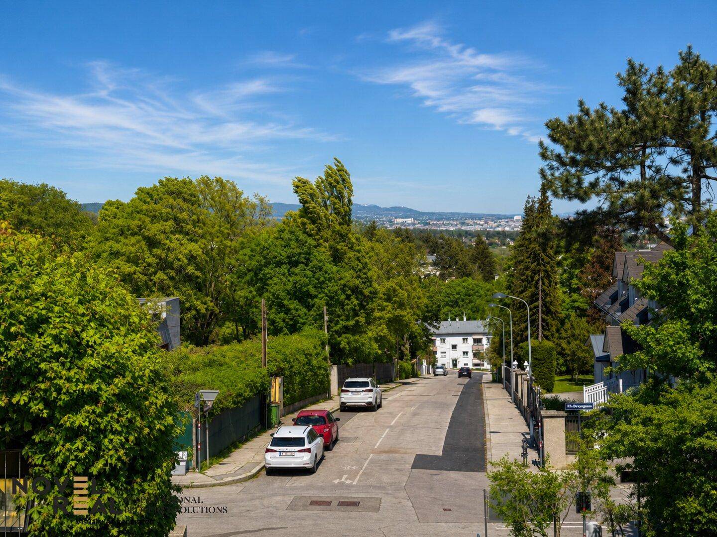 Ruhige Wohnstraße mit Bäumen und Häusern, die einen weiten Blick auf die Stadt und Berge bietet.