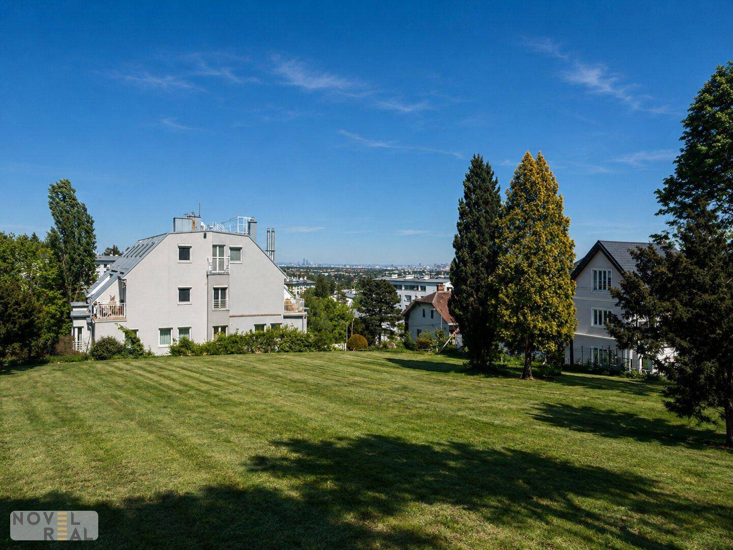 Weitläufige Rasenfläche mit Wohnhäusern und einem Panoramablick auf die Stadt in der Ferne.