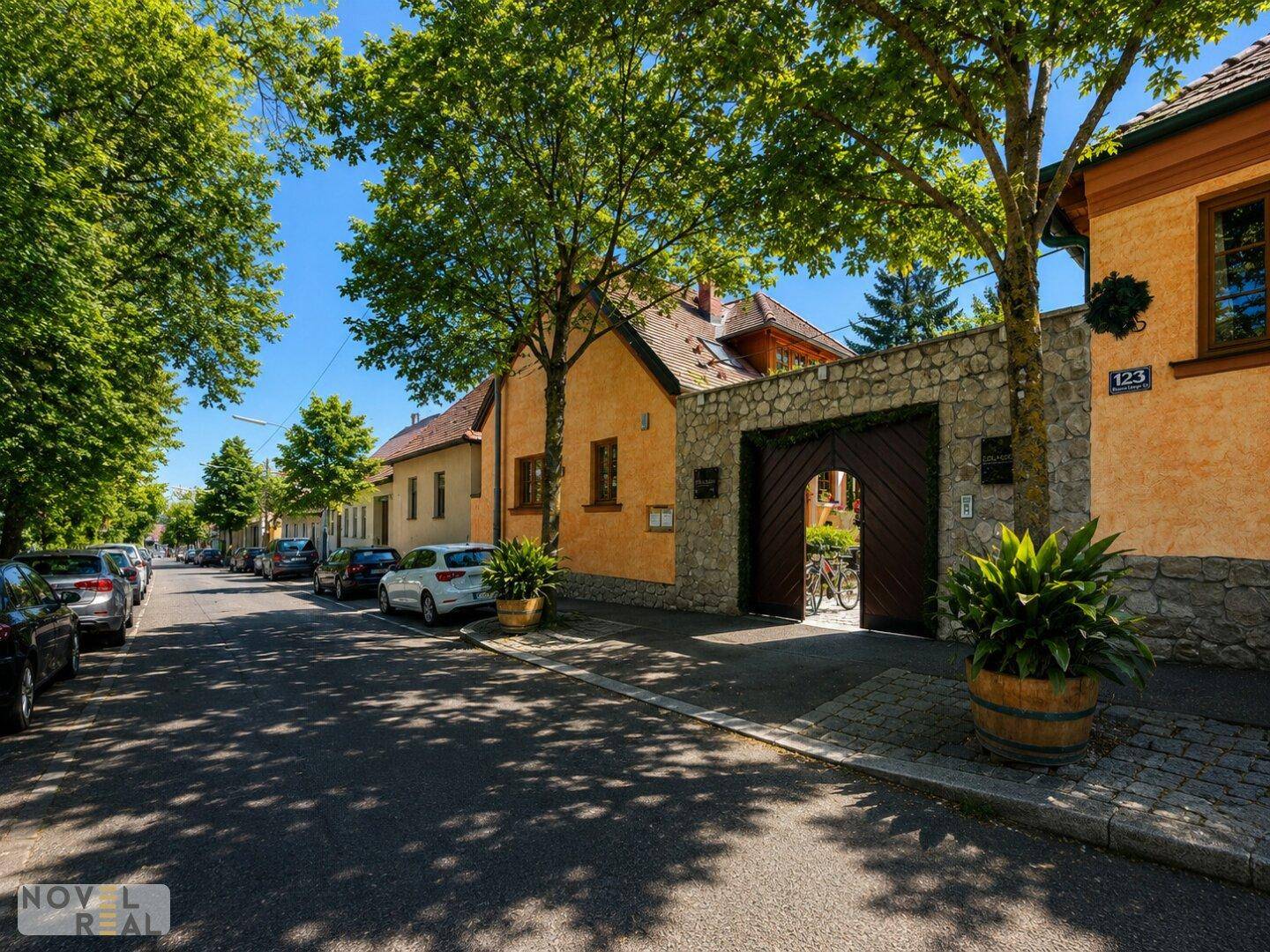 Ruhige Wohnstraße mit traditionellen Gebäuden und einem markanten Steintor unter Bäumen.