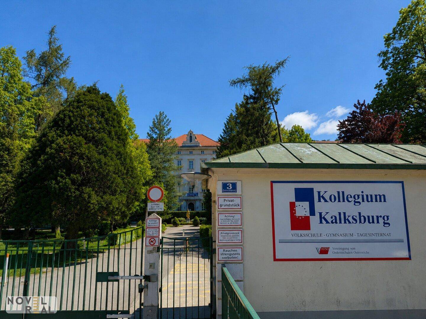 Eingangsbereich des Kollegiums Kalksburg mit Schild, Tor und altem Baumbestand.