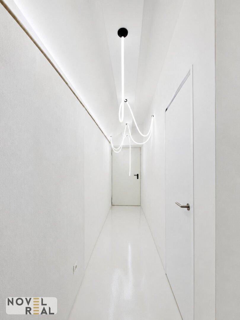 Schmaler, heller Flur mit minimalistischer Beleuchtung und weißen Türen, der eine moderne und saubere Ästhetik aufweist.