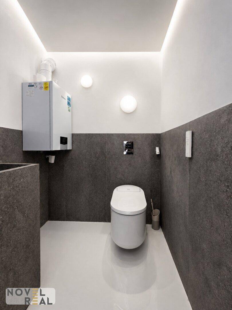 Modernes Gäste-WC mit dunklen Fliesen, einer wandmontierten Toilette und einem Heizkessel an der Wand.