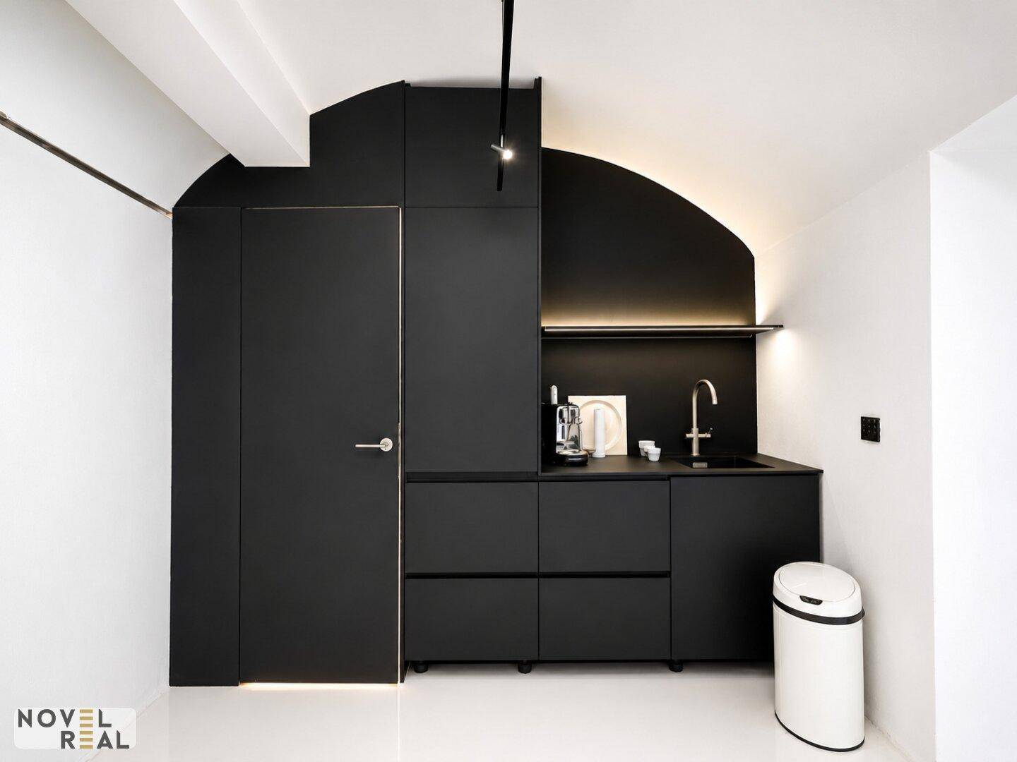 Elegante, minimalistische Küchenzeile in Schwarz mit integrierten Geräten und indirekter Beleuchtung unter einer gewölbten Decke.