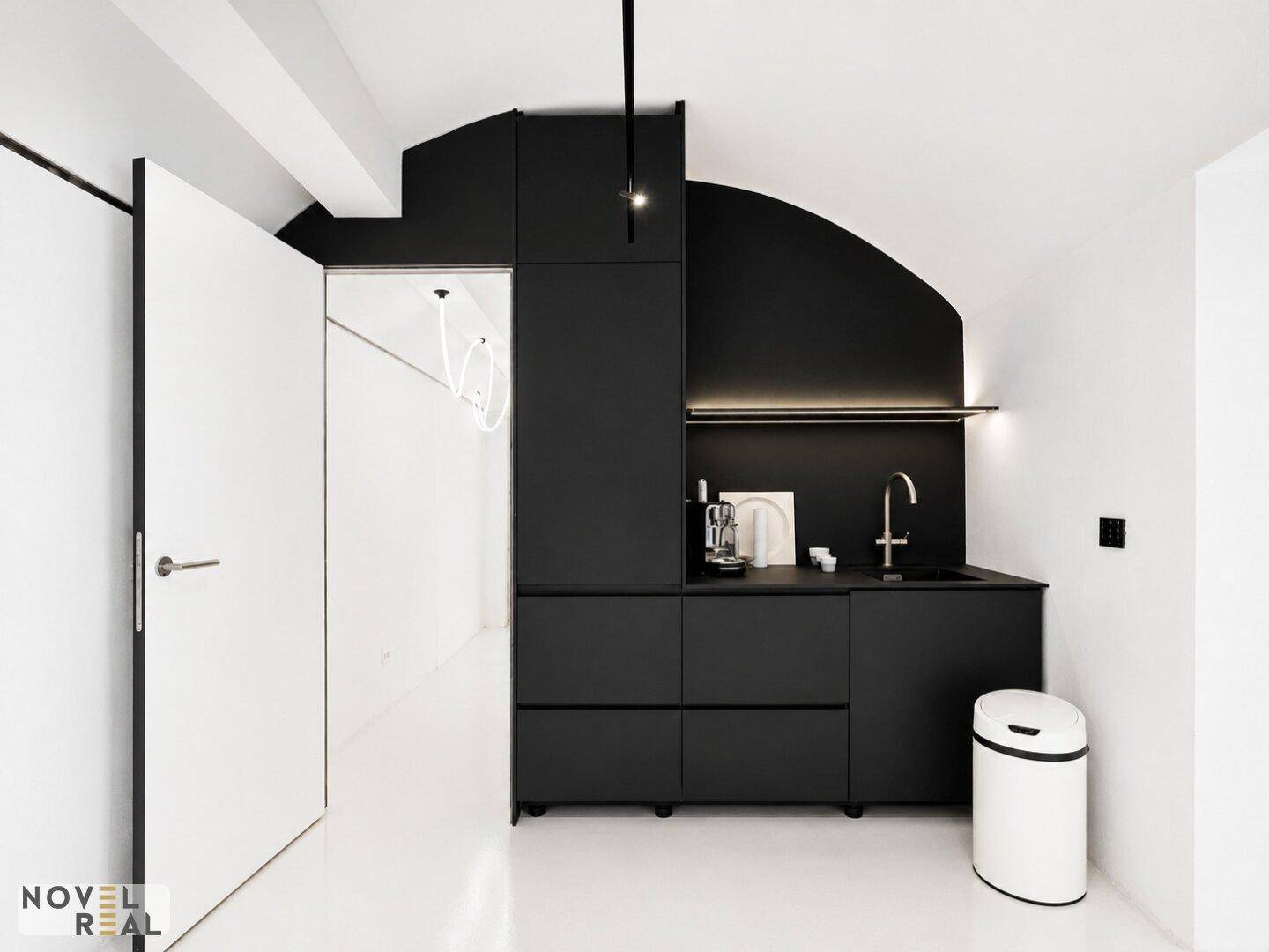 Moderne schwarze Küchenzeile mit integrierter Tür, Spüle und Kaffeemaschine in einem minimalistischen Raum mit gewölbter Decke.