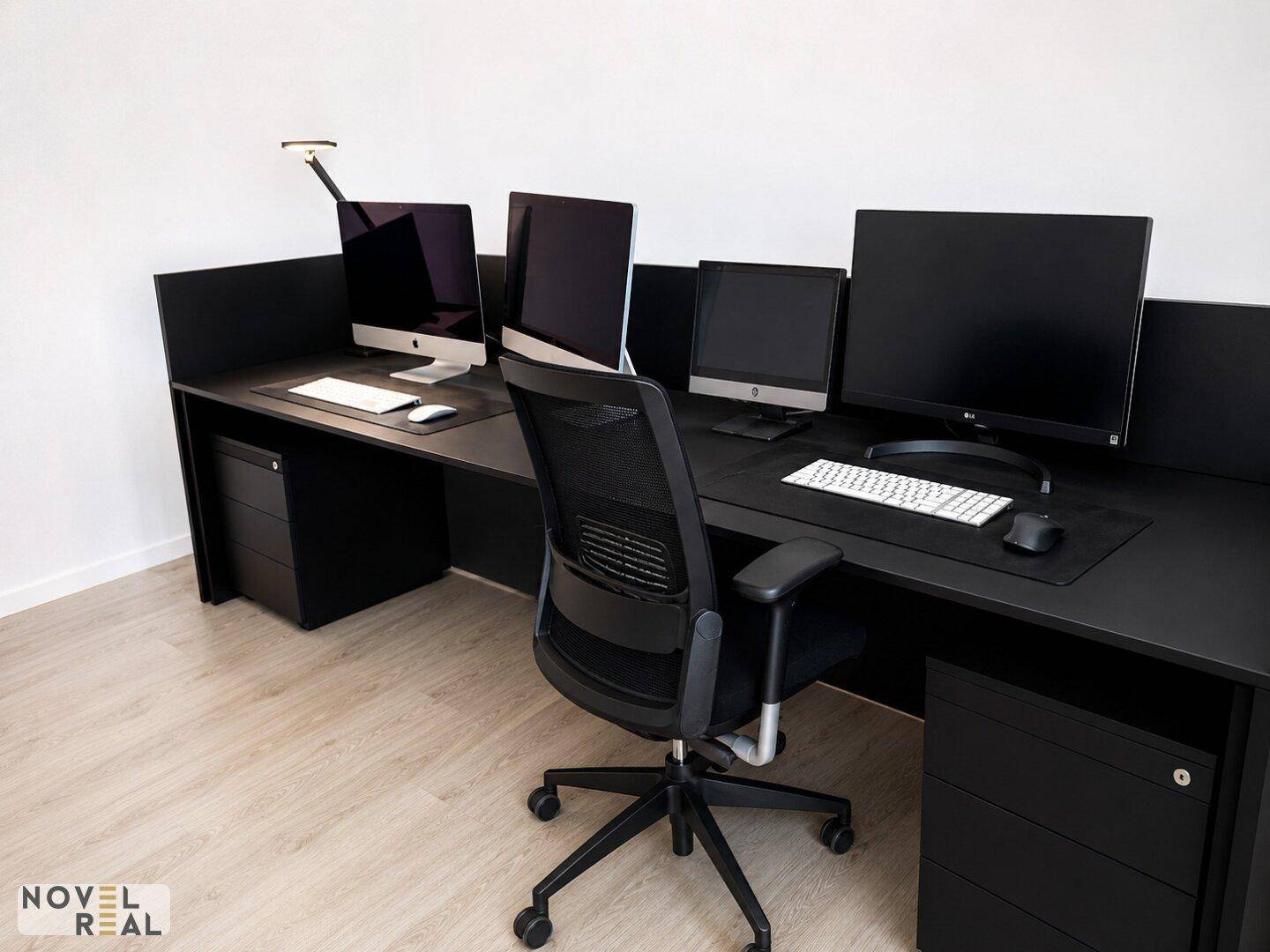 Moderner Arbeitsplatz mit schwarzen Schreibtischen, Computermonitoren und ergonomischen Stühlen in einem hellen Büro.