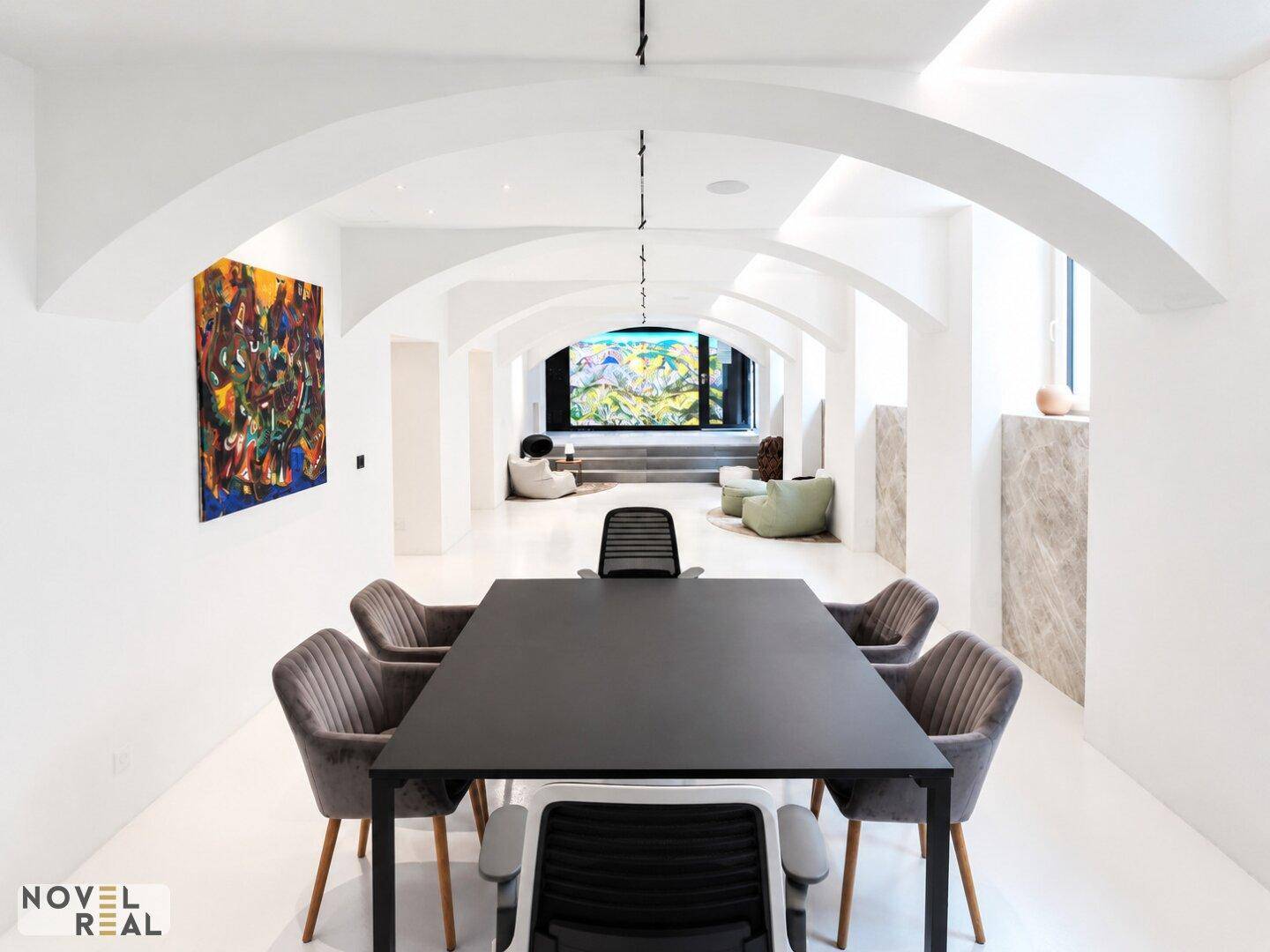Großer Konferenzraum mit einem schwarzen Tisch und grauen Stühlen, umgeben von gewölbten Decken und moderner Kunst.