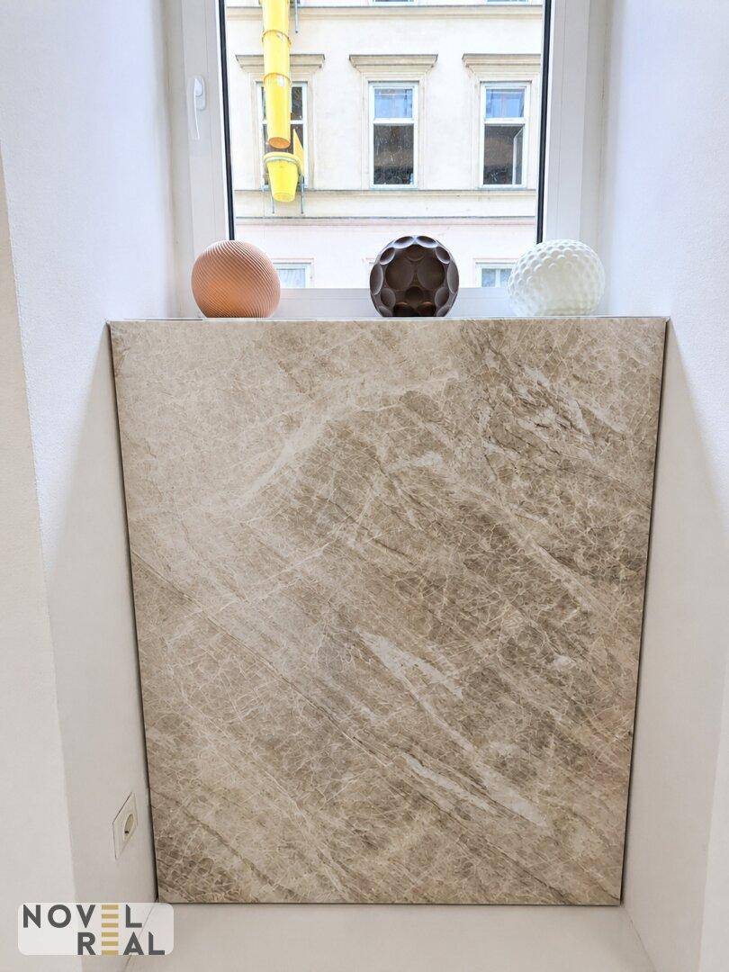 Fensterbereich mit einer Marmorverkleidung und dekorativen Kugeln, der einen Blick auf die gegenüberliegende Fassade bietet.