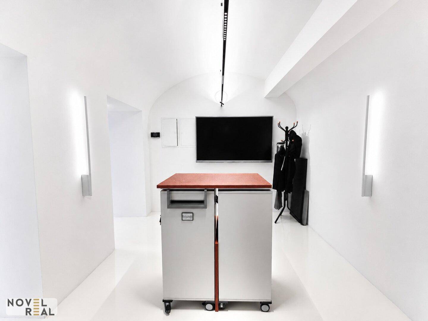 Langer, heller Flur mit einem mobilen Servierwagen und einem an der Wand montierten Fernseher in einem modernen Ambiente.