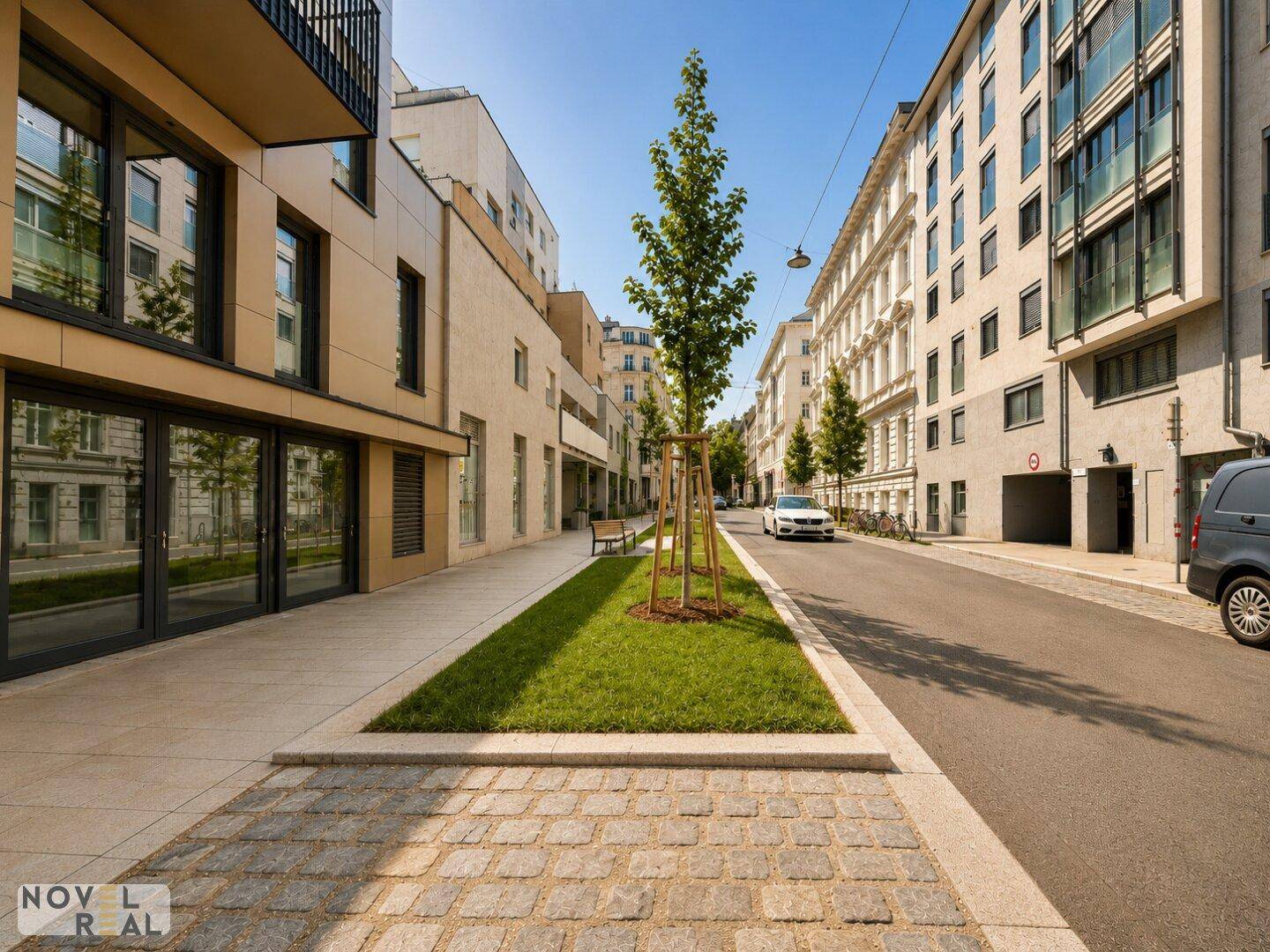 Moderne Wohngebäude und eine begrünte Straße mit Kopfsteinpflaster in einer städtischen Umgebung.