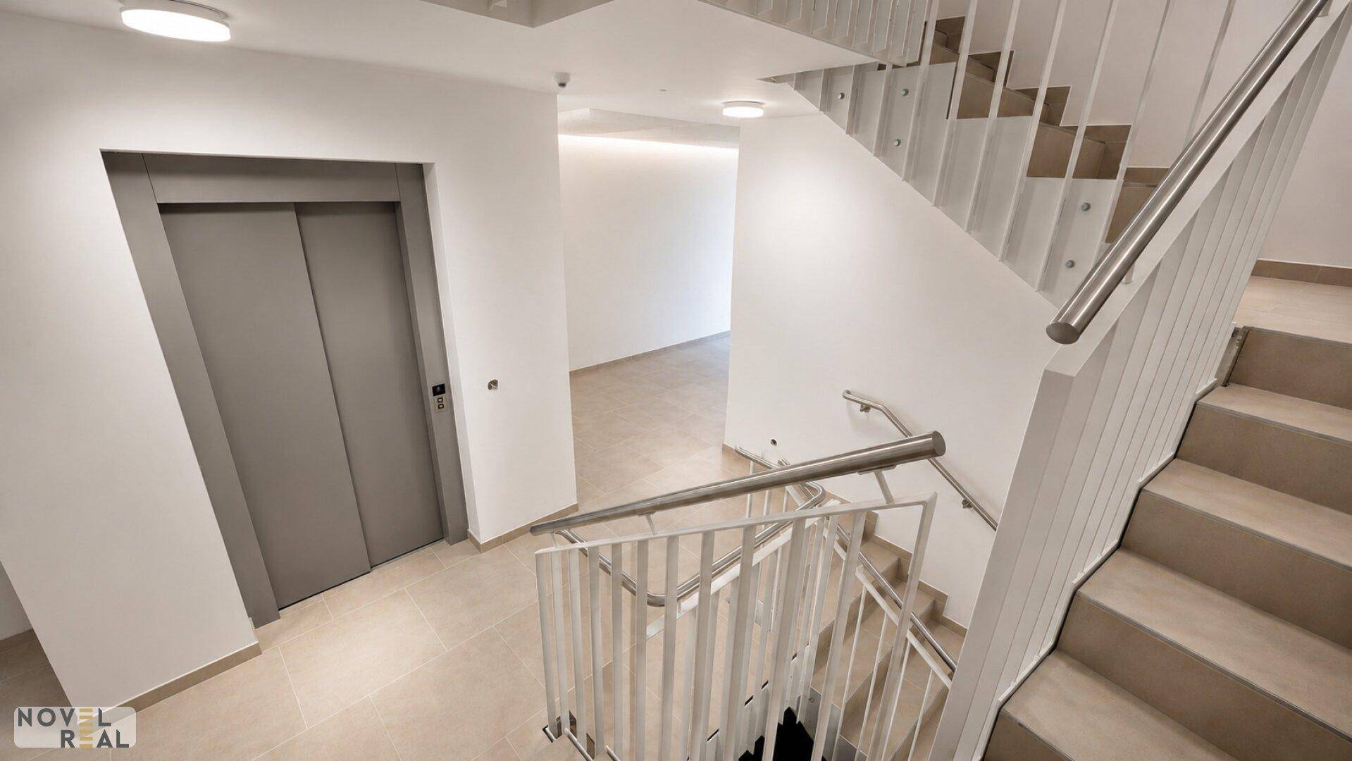 Modernes Treppenhaus mit Aufzug und hellem Fliesenboden im Eingangsbereich des Gebäudes.