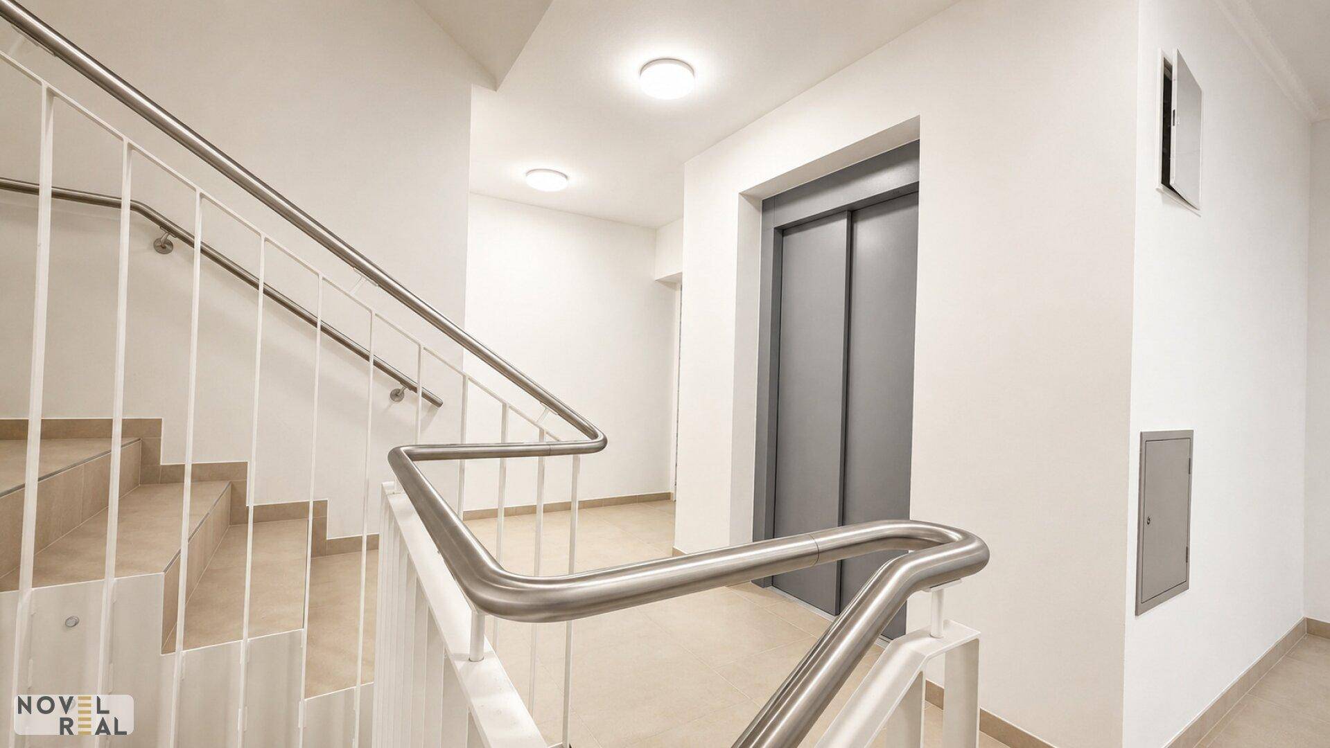 Heller Treppenaufgang mit Edelstahlgeländer und modernem Aufzug in einem Neubau.