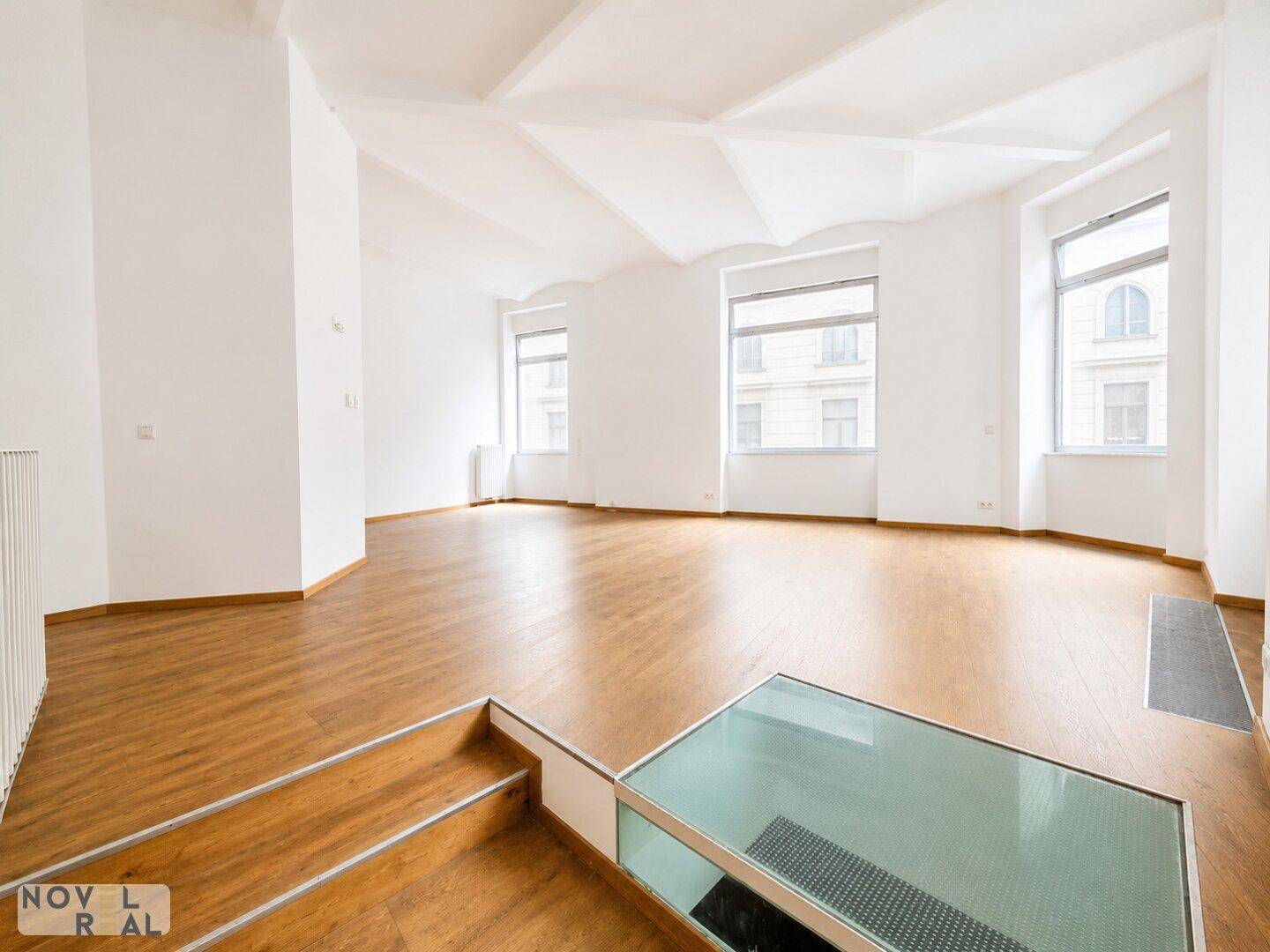Geräumiger, heller Raum mit Holzboden, hohen Decken und großen Fenstern, ideal für Wohn- oder Arbeitszwecke.