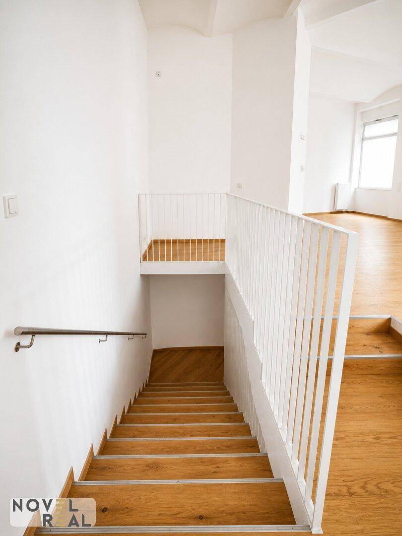 Moderne Holztreppe mit weißem Geländer, die verschiedene Ebenen des Gebäudes miteinander verbindet.