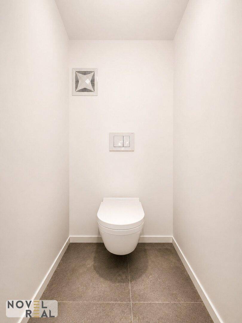 Modernes Gäste-WC mit wandhängender Toilette, grauen Fliesen und einem Abluftventilator.