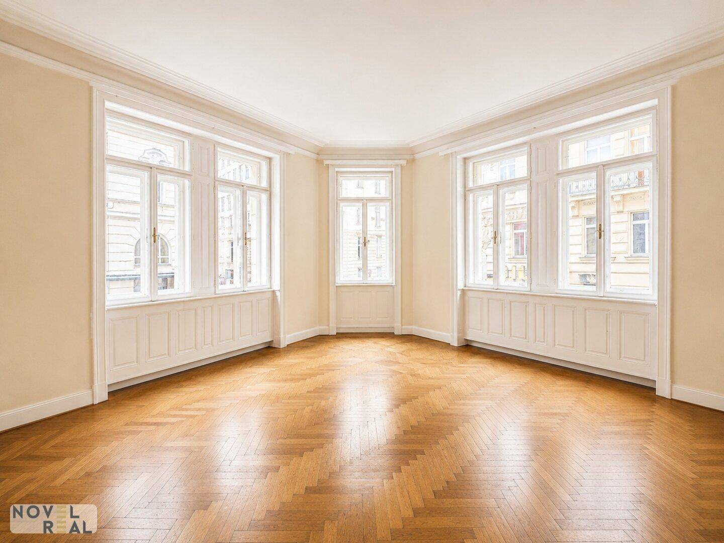 Geräumiges Zimmer mit Fischgrätparkett und vielen Fenstern, bietet viel Tageslicht.