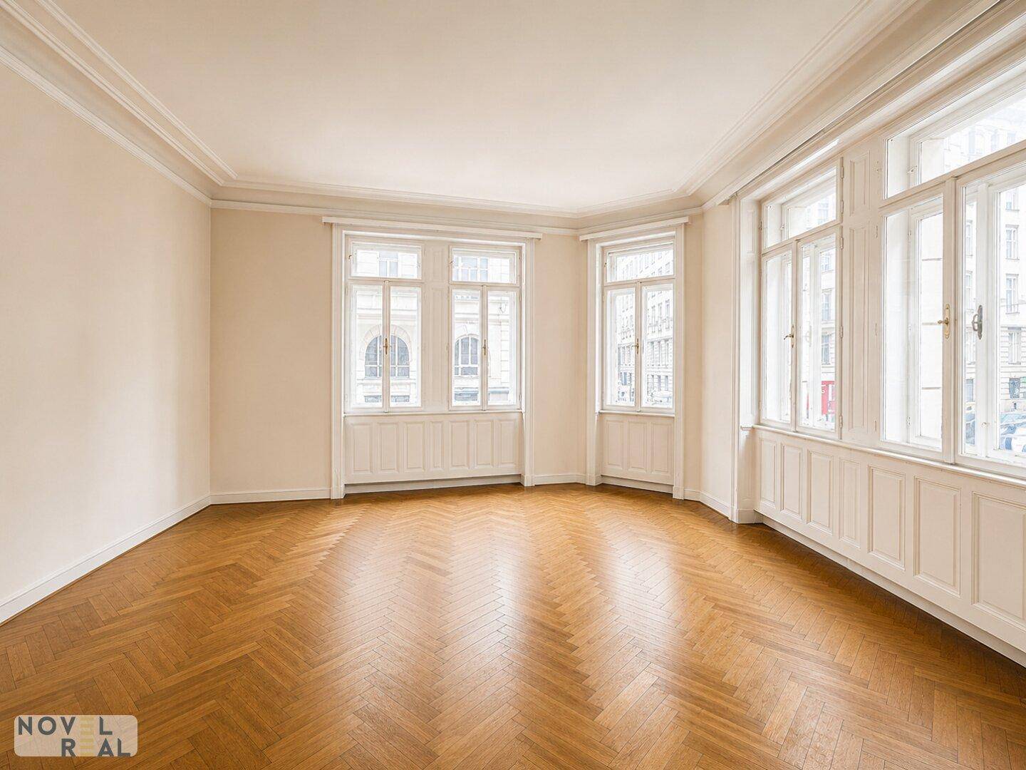 Geräumiges Zimmer mit Fischgrätparkett und hohen Fenstern, ideal für Wohnzwecke.
